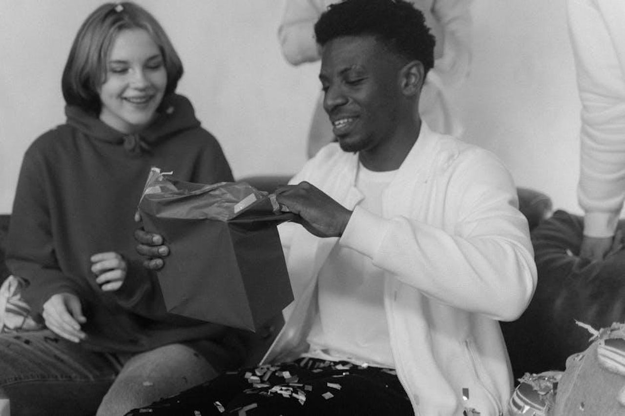 Gizelle_Bryant_e_Altre_Reazioni_alla_Sentenza_HL4Oi6cTAC - Confidenze24 Source: Tima Miroshnichenko - pexels - A man joyfully opens a gift surrounded by friends in a monochrome setting.