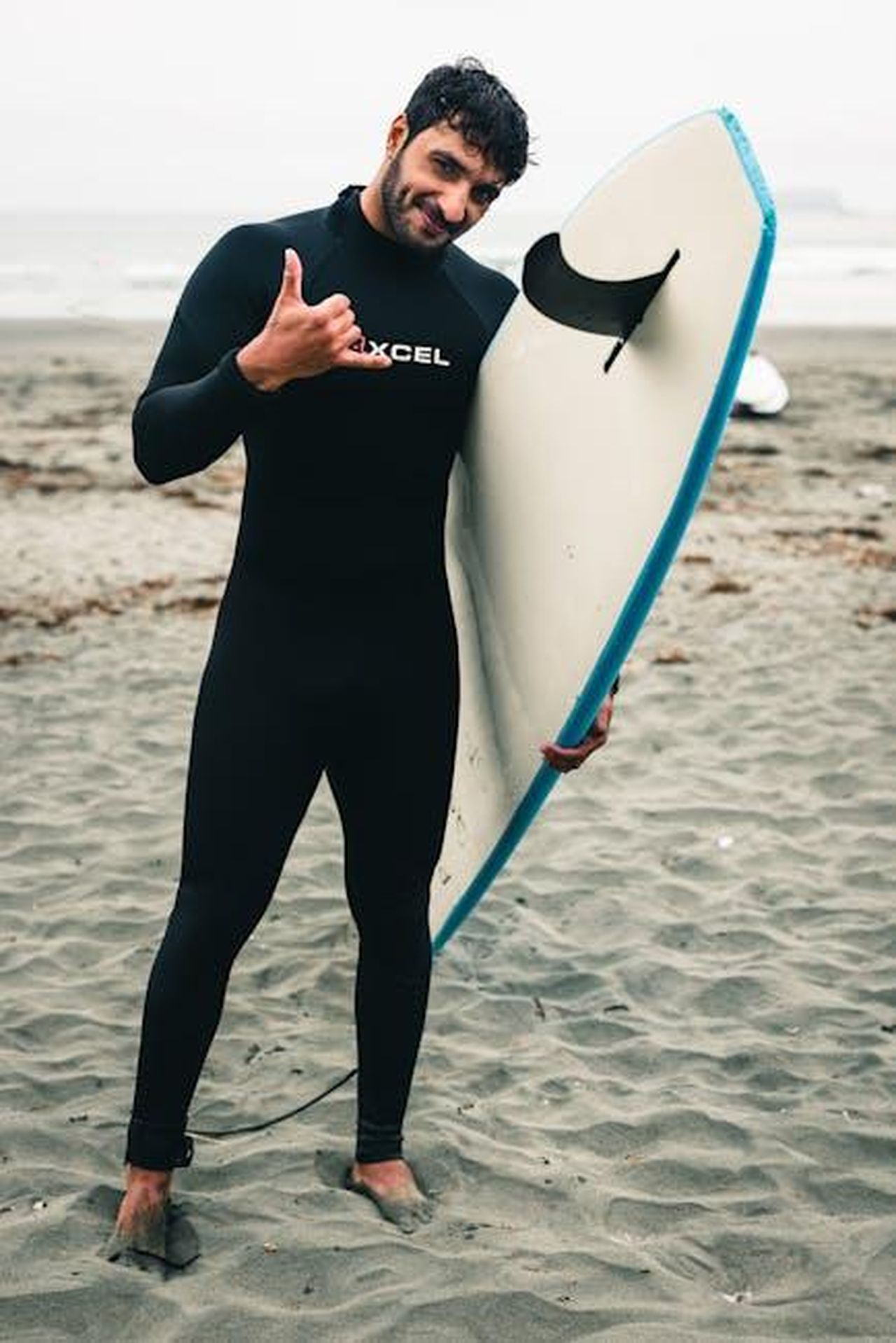 Grace_e_le_sue_avventure_con_il_surf_JUbGE6qavh - Confidenze24 Source: Ali Kazal - pexels - A cheerful surfer poses with his surfboard on Tofino Beach, ready for adventure.