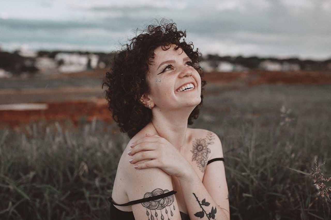 Grassa_ma_pi_felice_che_mai_OTLb802WxW - Confidenze24 Source: Gabriela Cheloni - pexels - A smiling woman with tattoos enjoys the outdoors in Maringá, Brazil, exuding happiness and warmth.