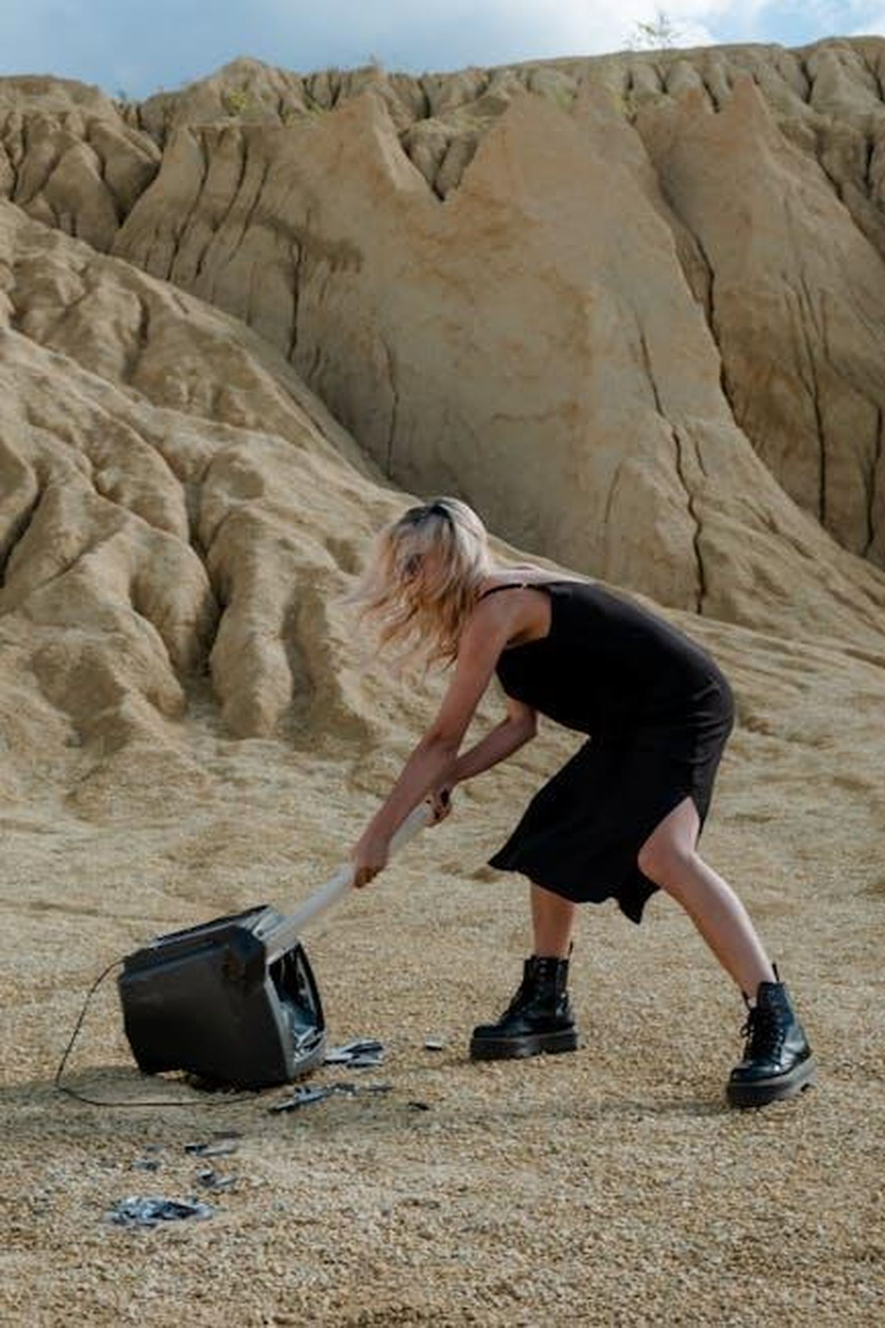 Hope_e_Taylor_Frankie_Paul_erano_amiche_intime_6OeY7DSwzO - Confidenze24 Source: cottonbro studio - pexels - A woman in a black dress breaks a TV with a sledgehammer in a desert landscape.