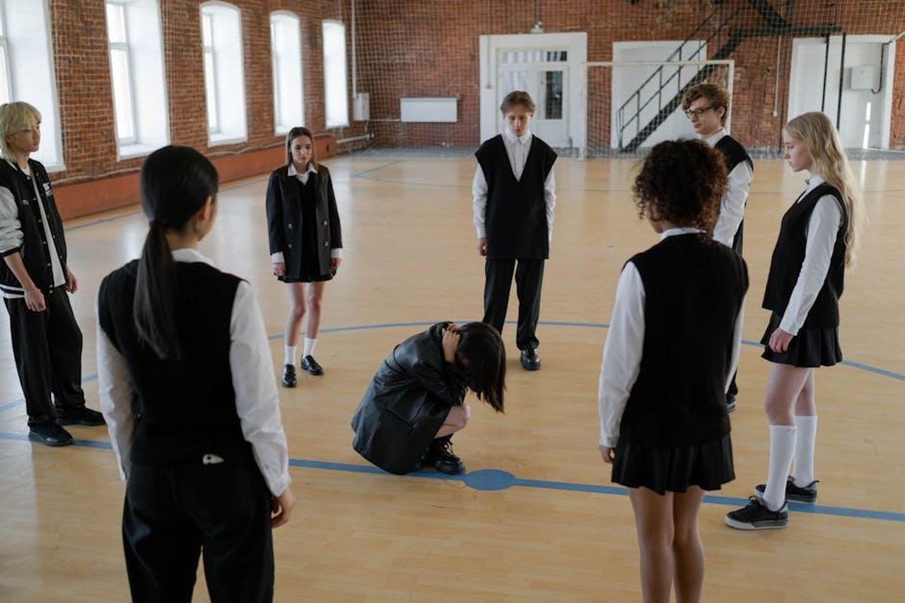 Hope_e_Taylor_Frankie_Paul_erano_amiche_intime_yus2BT4ruZ - Confidenze24 Source: cottonbro studio - pexels - A group of teenagers in school uniforms gather around a peer in a gym setting, depicting peer dynamics.
