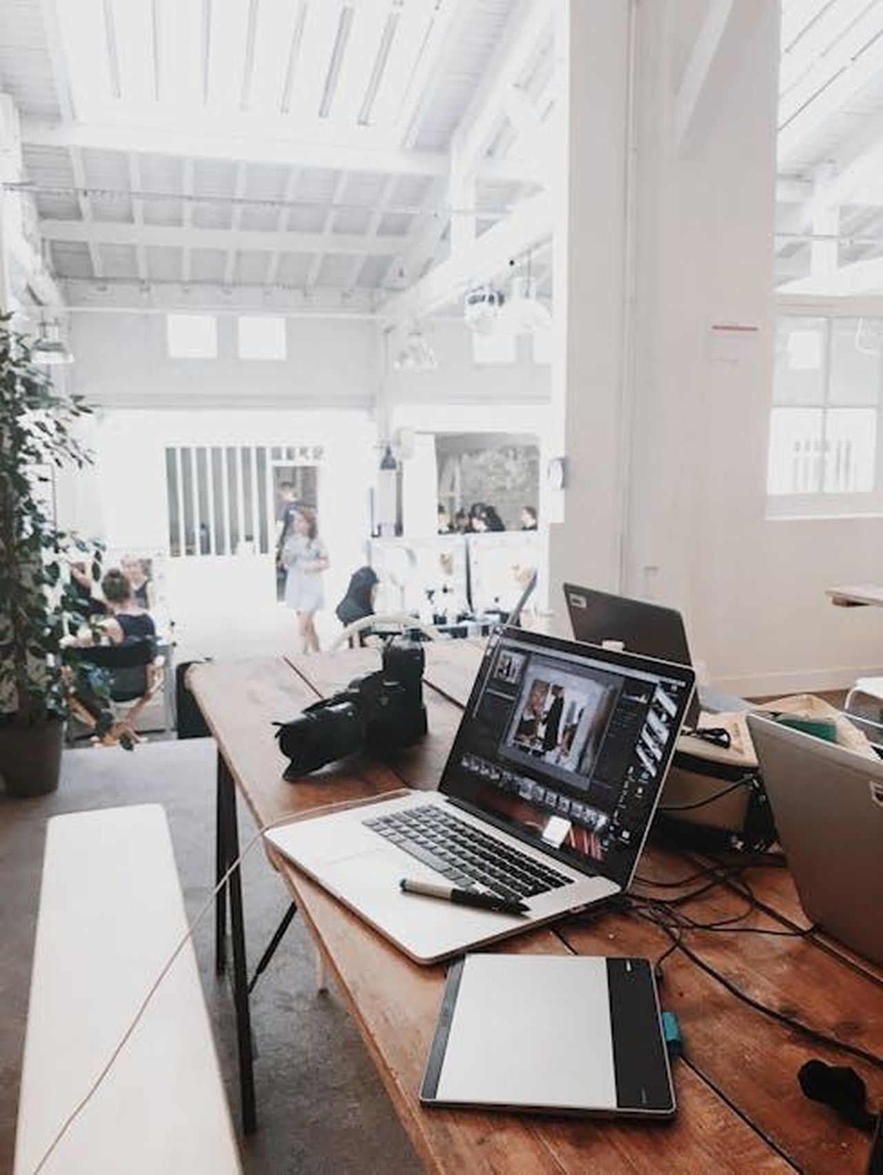 I_benefici_dei_media_digitali_KFzImFsiYn - Confidenze24 Source: Flo Dahm - pexels - A bright, modern workspace featuring laptops, a camera, and a drawing tablet in an indoor office.