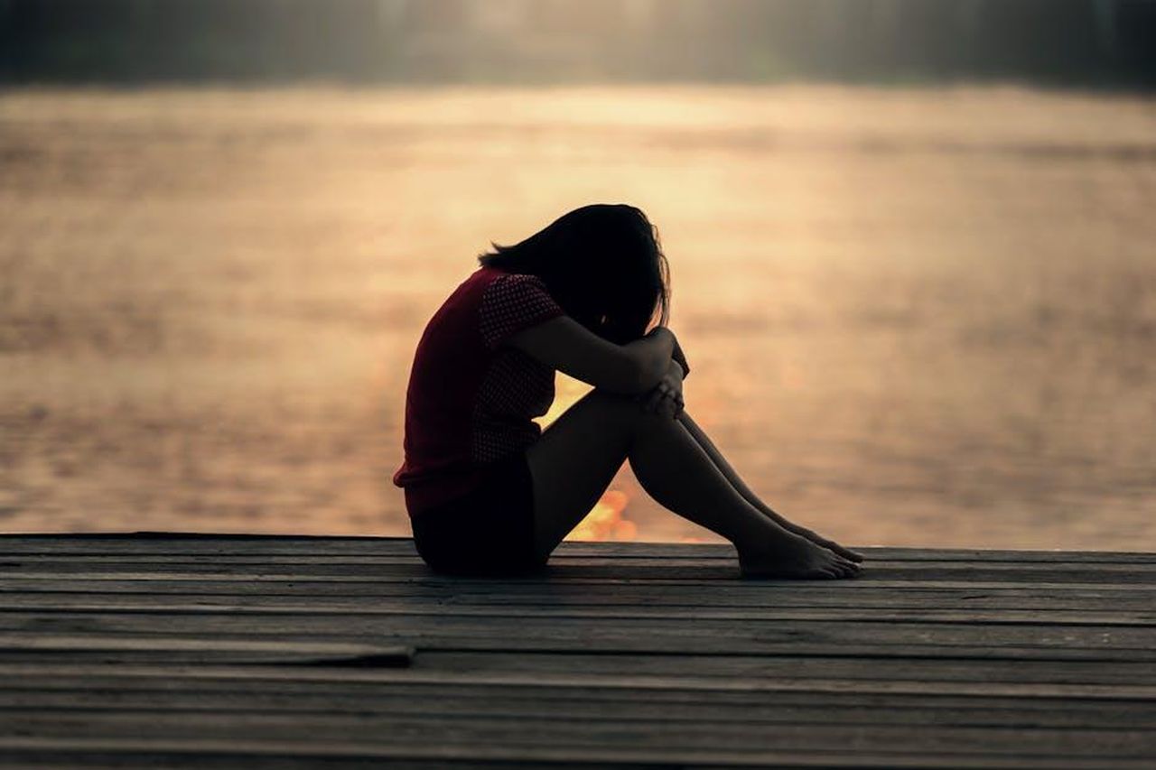 I_fan_condividono_il_loro_dolore_9oENV5jegK - Confidenze24 Source: Pixabay - pexels - A woman sitting alone on a wooden dock by the lake, showing solitude and reflection.