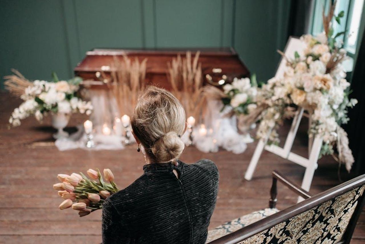 I_fan_inviano_messaggi_di_auguri_G2fv81rxwV - Confidenze24 Source: Pavel Danilyuk - pexels - A woman mourns at an indoor funeral ceremony with floral decorations and a coffin.