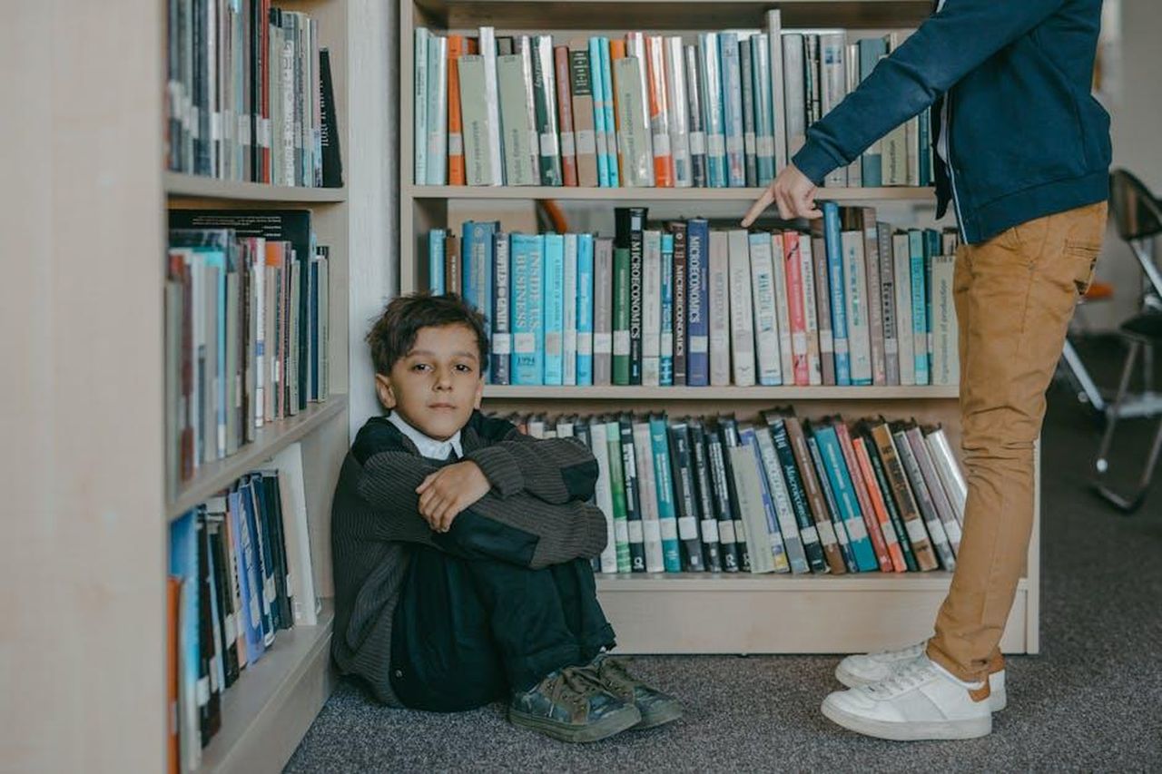 Il_Commento_Sorprendente_di_Ryan_Seacrest_YpBtlqWoZj - Confidenze24 Source: Mikhail Nilov - pexels - A sad boy sitting on the library floor while being bullied by a peer.