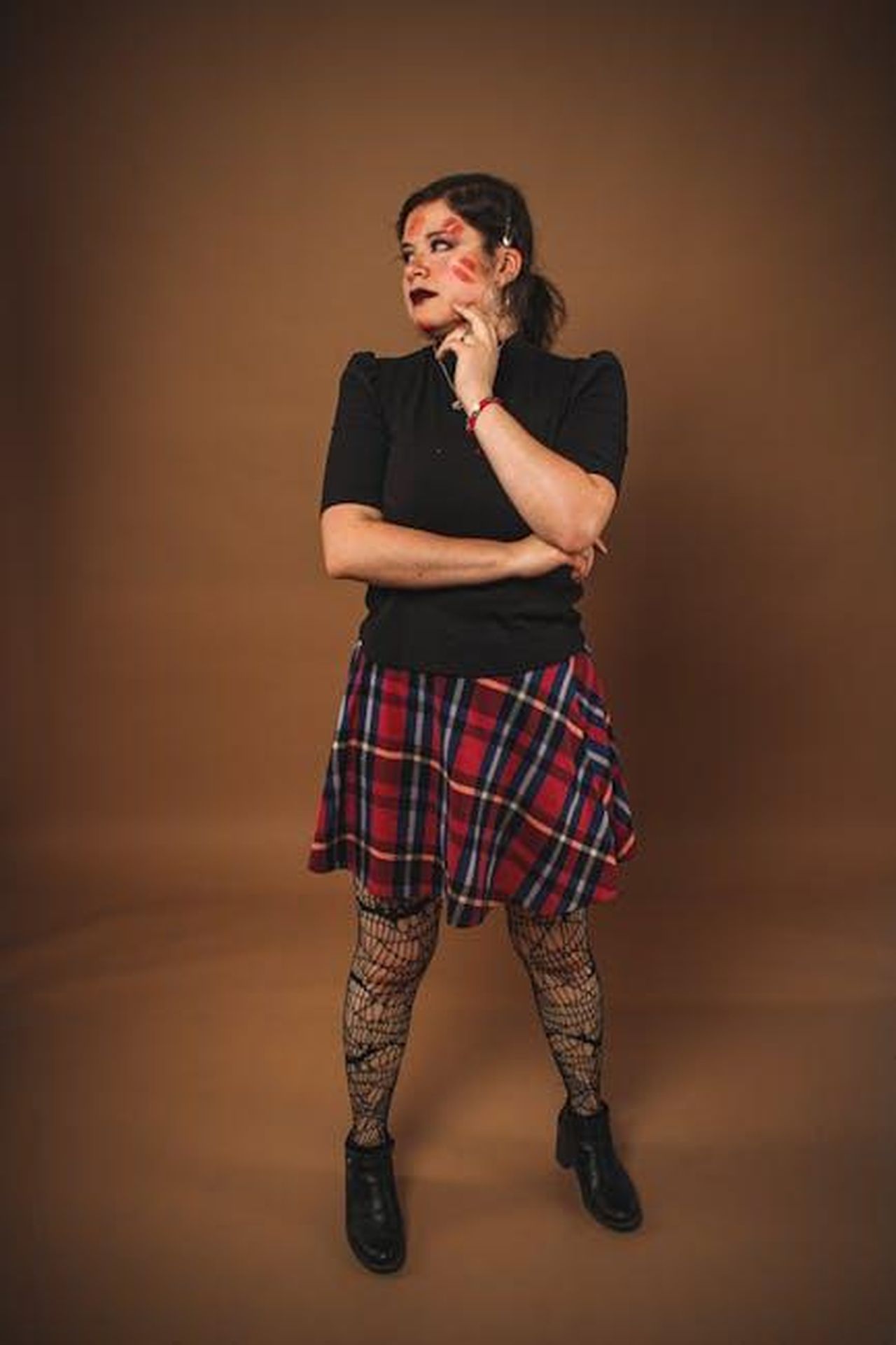 Il_bacio_ai_BRITs_e_le_conseguenze_Ee94WHOYdL - Confidenze24 Source: Moisés Fonseca - pexels - Stylish woman in plaid skirt and fishnet stockings posing confidently in a studio setting.