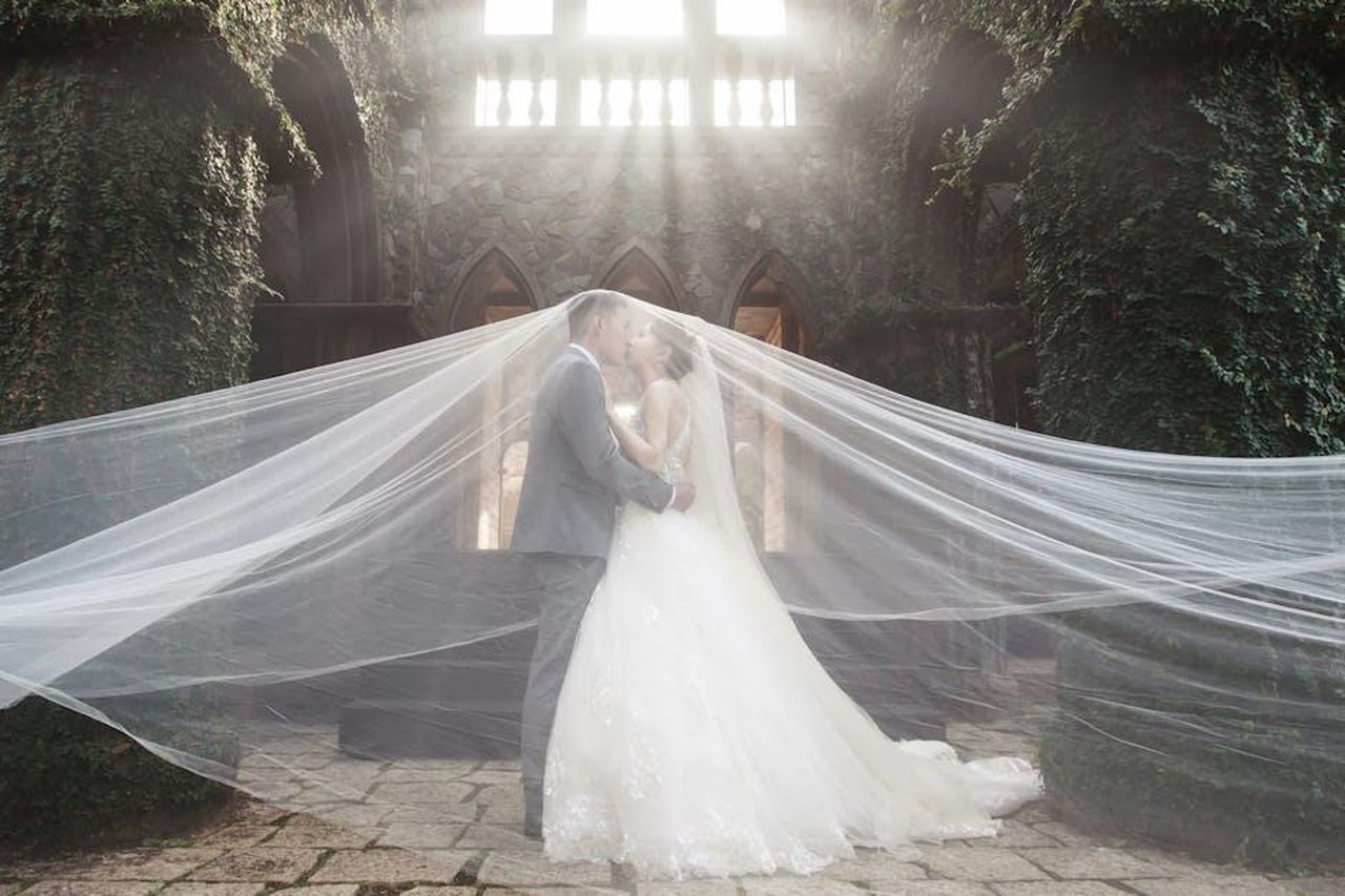 Il_bacio_brillo_di_Danny_e_Maura_RNpvkLYQOi - Confidenze24 Source: 嵐 楓 - pexels - A romantic wedding scene with a couple kissing under dramatic lighting at an ivy-covered stone structure.