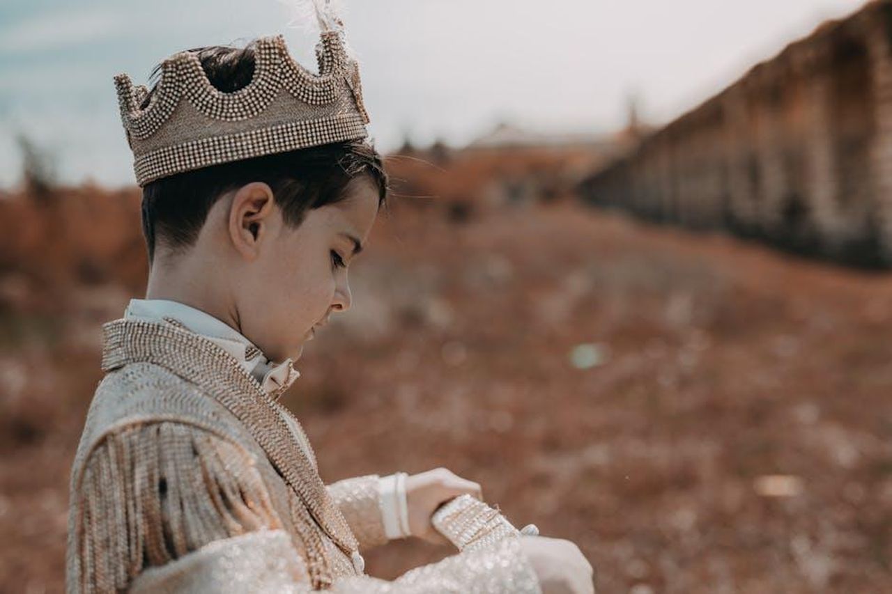 Il_cambiamento_dello_stile_di_Harry_in_California_KGcJRyGZWP - Confidenze24 Source: R. Fera - pexels - A child dressed as a prince wearing a crown in an outdoor setting with fall scenery.
