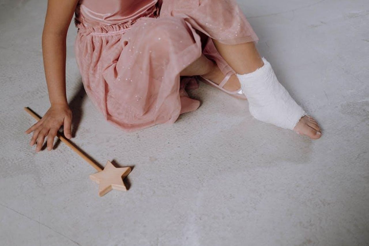 Il_cast_stellare_di_The_Residence_v7jwxrkOW2 - Confidenze24 Source: cottonbro studio - pexels - Close-up of a child's injured foot with cast, wearing a pink dress and holding a magic wand.