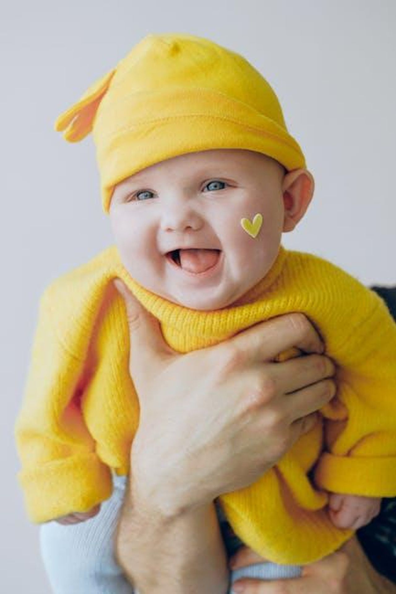 Il_divertente_alter_ego_di_Melissa_Midway_Mom_m1kzs5x1YX - Confidenze24 Source: Anna Shvets - pexels - Adorable baby wearing a yellow beanie with a heart sticker, smiling joyfully indoors.