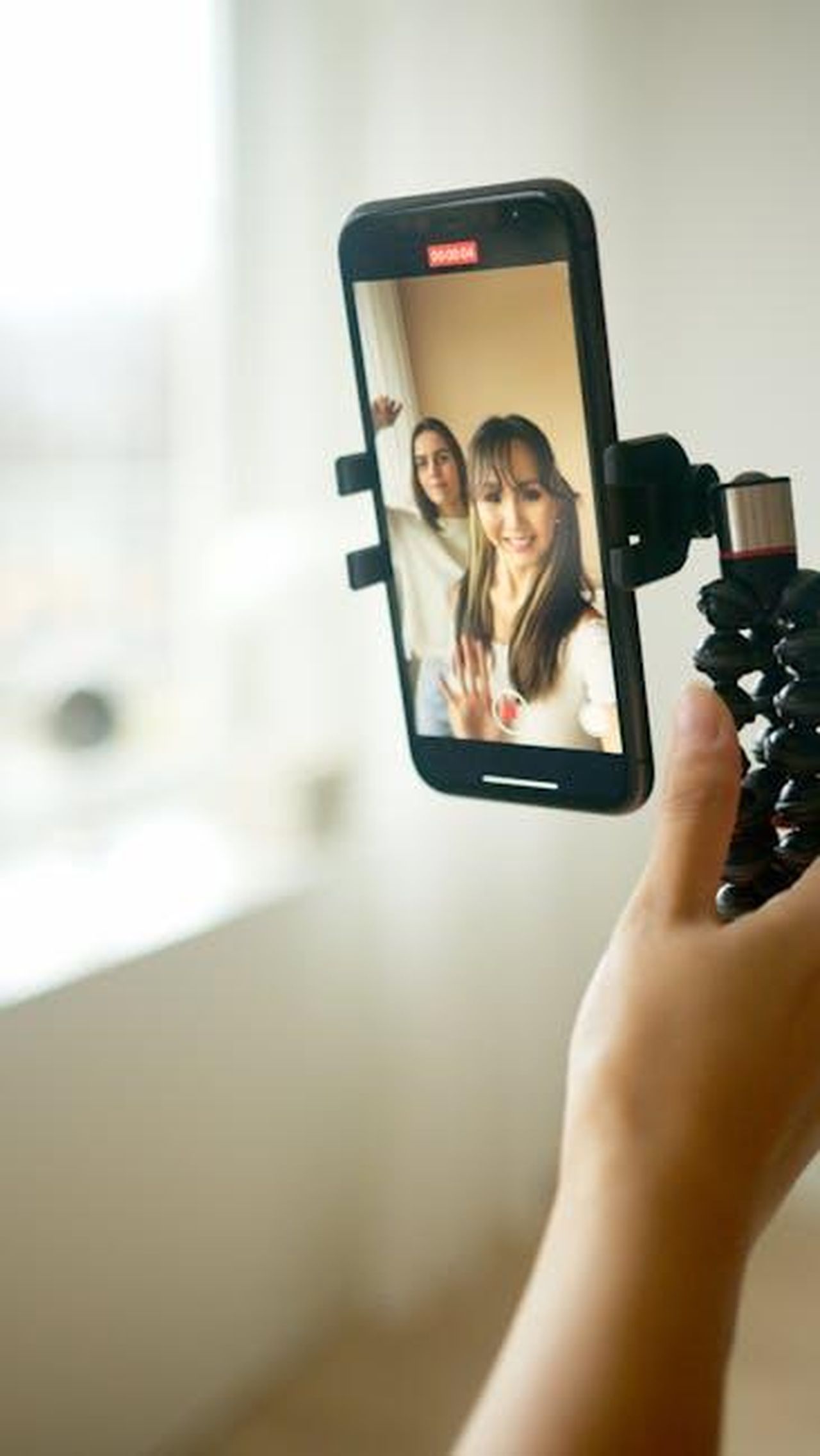 Il_filtro_chubby_e_il_suo_impatto_sui_giovani_S9Godruzve - Confidenze24 Source: Artem Podrez - pexels - Two young women are taking a joyful selfie using a smartphone indoors, capturing a happy moment.