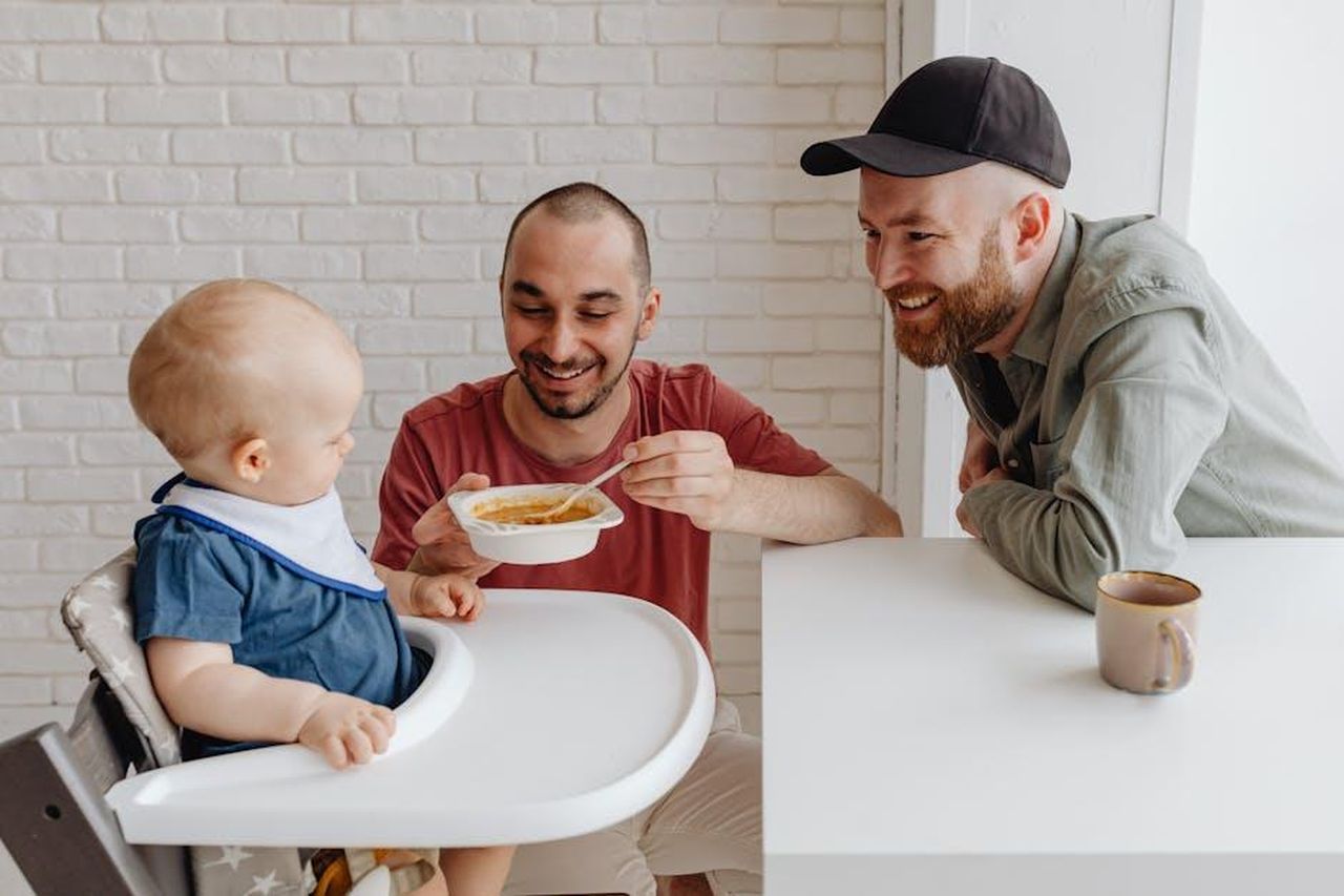 Il_lavoro_di_squadra_nella_genitorialit_L4ai2QLMoR - Confidenze24 Source: Photo By: Kaboompics.com - pexels - A joyful moment as two fathers feed their baby at home, showcasing love and family bonding.