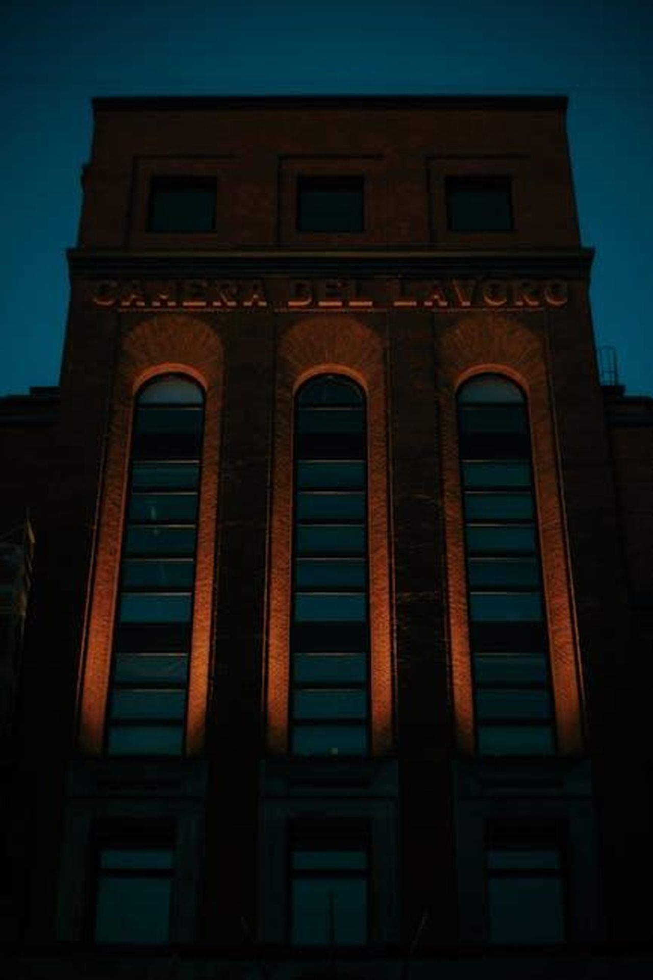 Il_lavoro_e_la_dedizione_di_Michael_Caine_TiXAQlTGdX - Confidenze24 Source: Francesco Ungaro - pexels - A tall brick building with arched windows illuminated at night, showcasing architectural elegance.