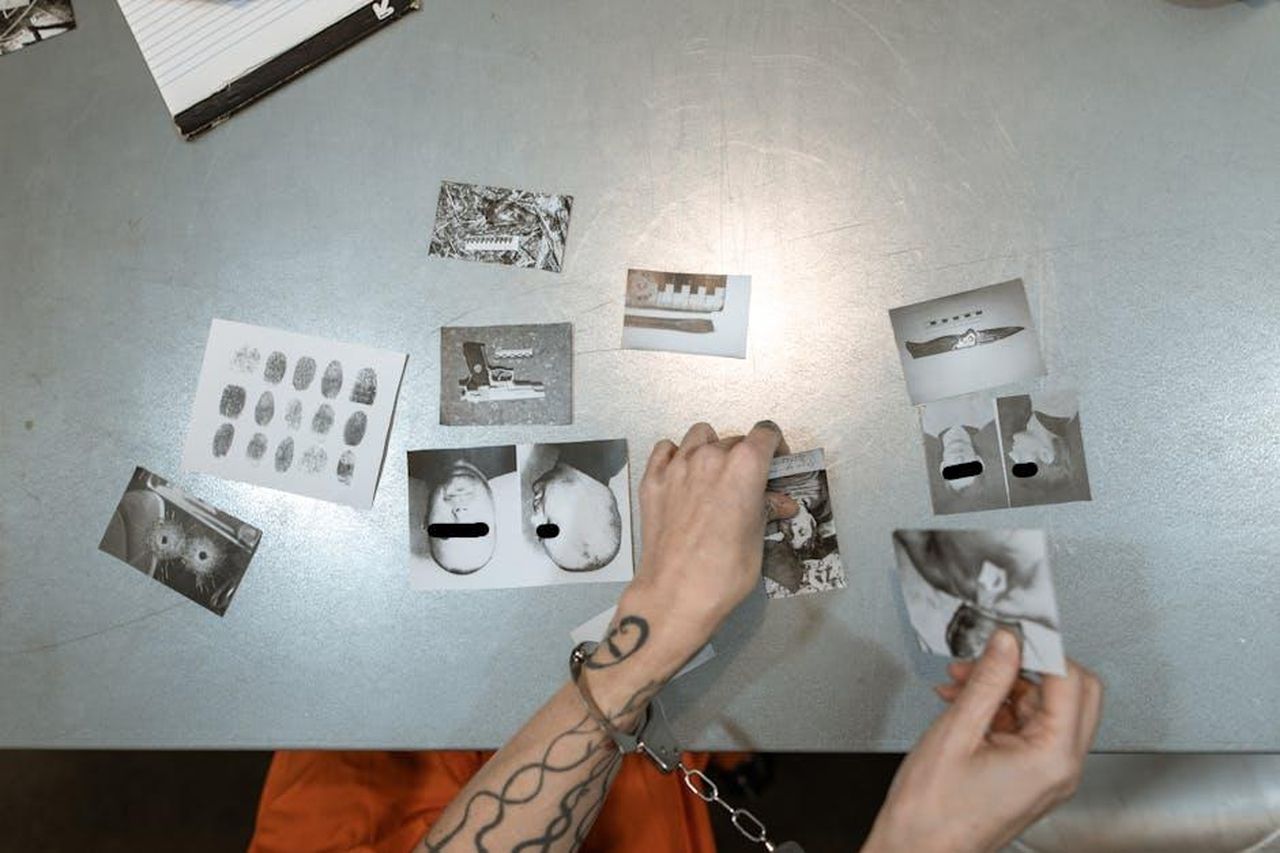 Il_matrimonio_avviene_dopo_uno_scandalo_2M8vV5nQ8S - Confidenze24 Source: RDNE Stock project - pexels - A handcuffed person examines evidence photos on a table, indicating a crime investigation scene indoors.