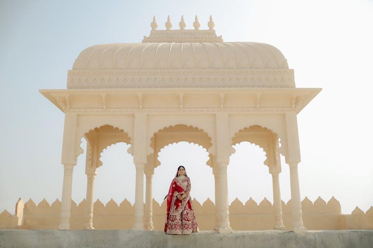 Il_matrimonio_di_Lady_Diana_un_evento_iconico_HBIONc3v8P - Confidenze24 Source: Fotographiya Wedding Photography - pexels - A traditional Indian bride poses elegantly at an ornate pavilion in bright daylight.