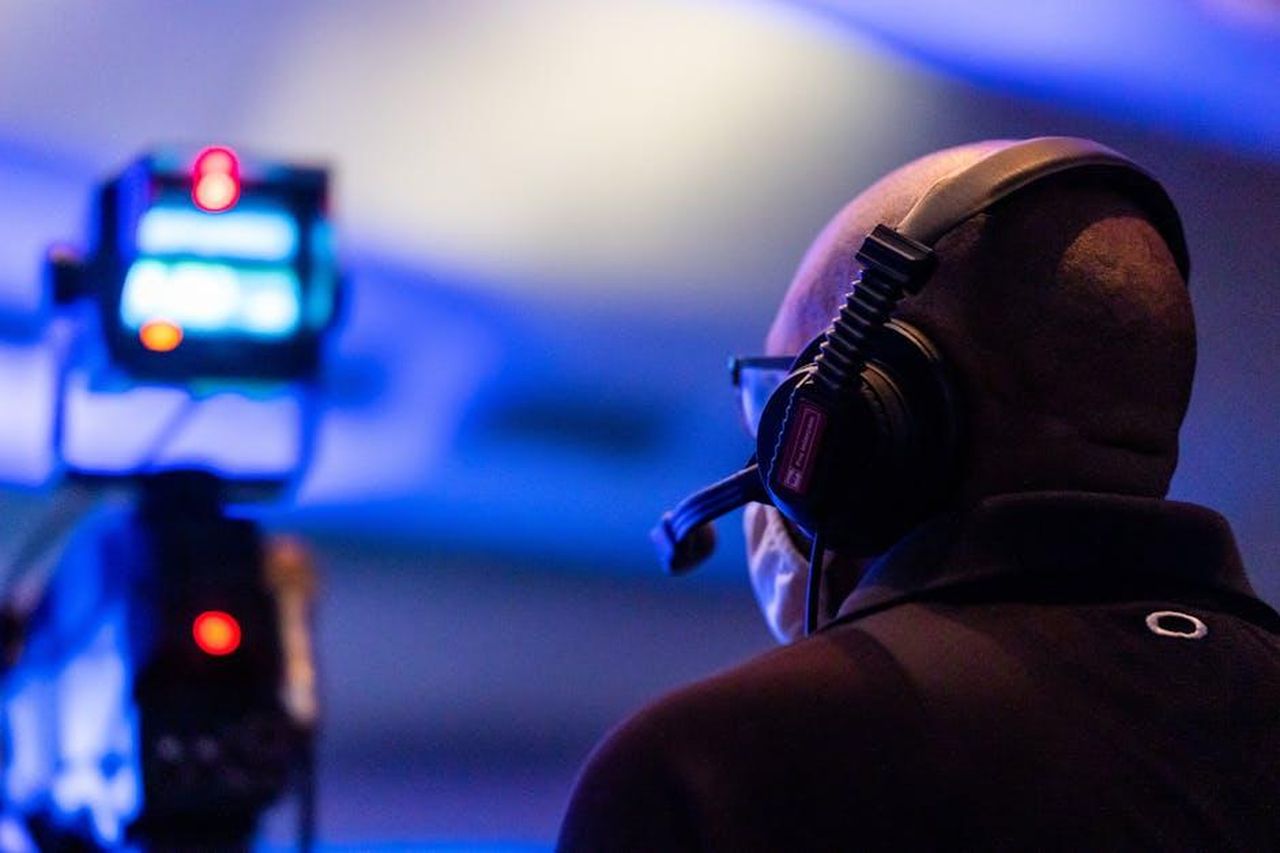 Il_percorso_di_Michael_Fishman_in_Roseanne_e_The_Conners_hKBjkogFDx - Confidenze24 Source: Caleb Oquendo - pexels - A bald man with a headset overseeing a live event in a dimly lit environment with a blurred camera in the foreground.