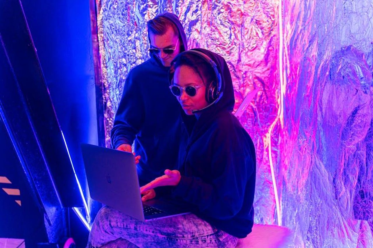 Il_pericolo_dellAI_per_i_creatori_bKXGxxAYY9 - Confidenze24 Source: Antoni Shkraba - pexels - Two individuals in a neon-lit room work on a laptop, showcasing modern technology themes.