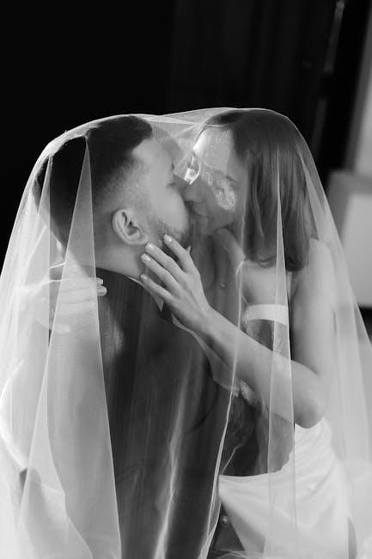 Il_primo_bacio_di_Jenna_e_Henry_K8dcR2OdCI - Confidenze24 Source: Alina Matveycheva - pexels - Bride and groom share a loving kiss under the veil, captured in timeless black and white.