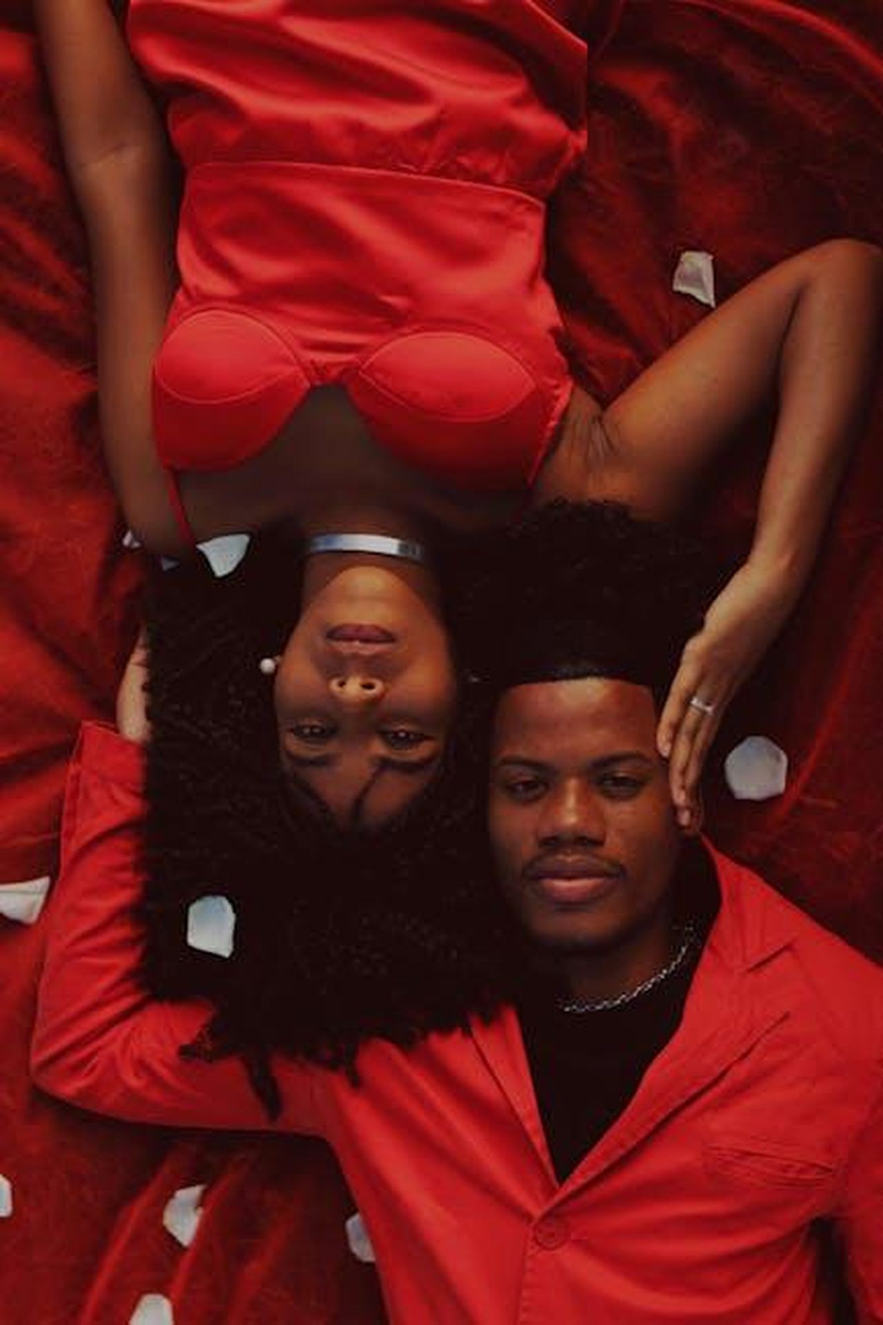 Il_ruolo_degli_intimacy_coordinator_sul_set_gu0lcGQb4M - Confidenze24 Source: Iury Bessa - pexels - Portrait of an African American couple lying on red fabric with petals, showcasing love and fashion.