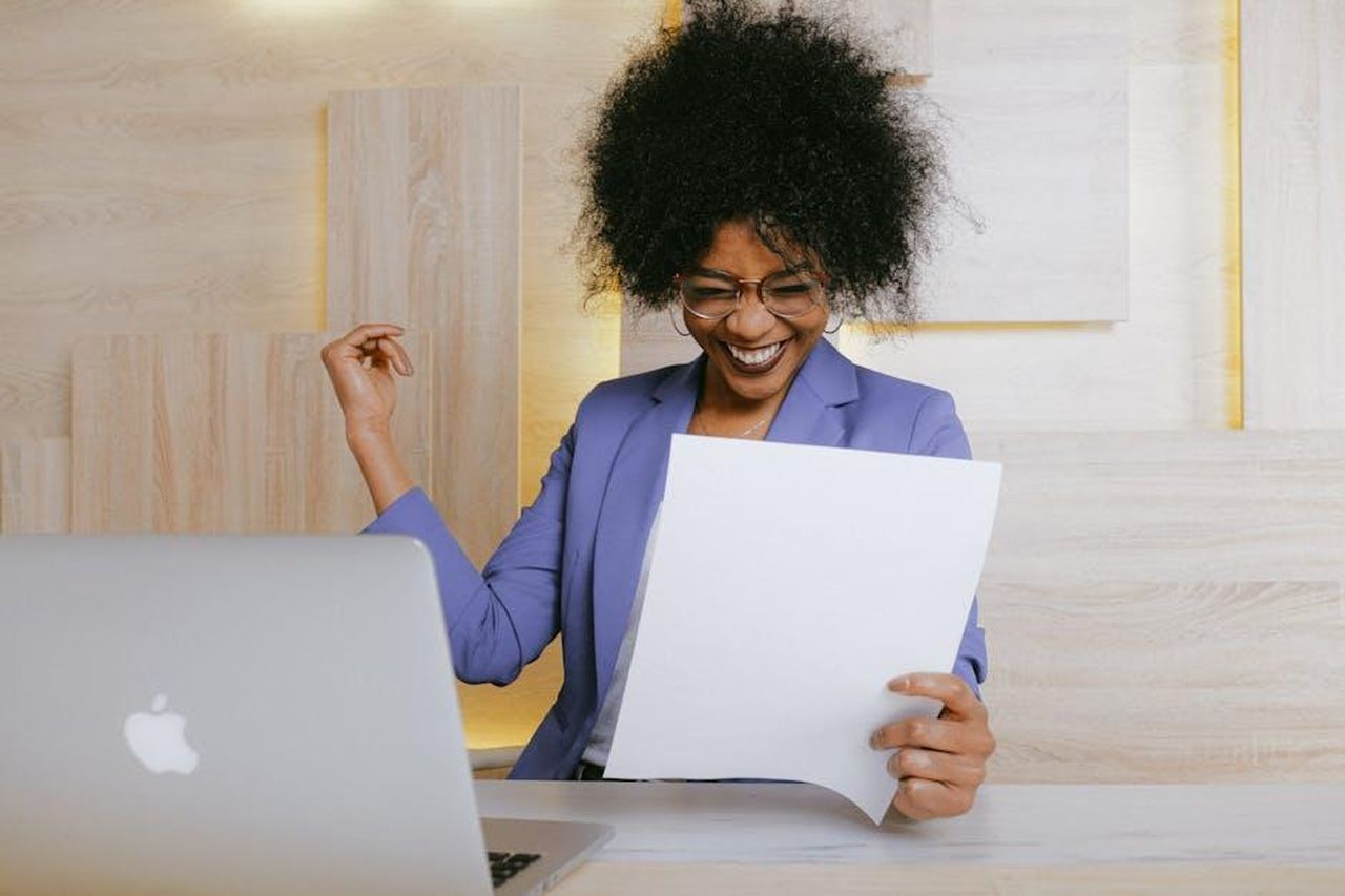 Il_ruolo_del_manager_di_Meghan_VV6MGnk0GD - Confidenze24 Source: Anna Shvets - pexels - A cheerful woman celebrates her success at work, looking at a document in an office setting.
