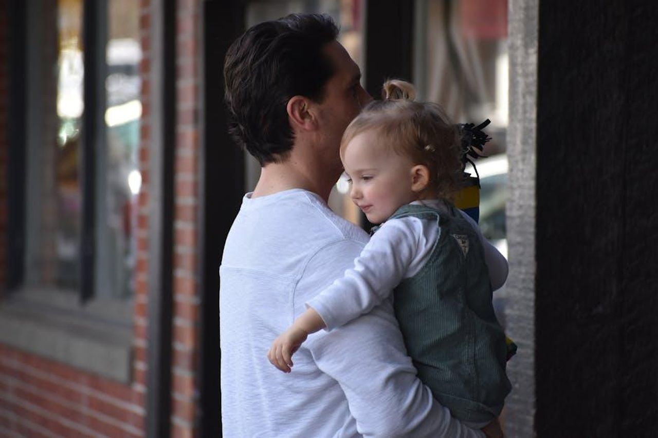 Il_ruolo_del_padre_nella_famiglia_moderna_vPcafyhkR9 - Confidenze24 Source: wr heustis - pexels - Father holding daughter outdoors, showcasing family bond in a city environment.
