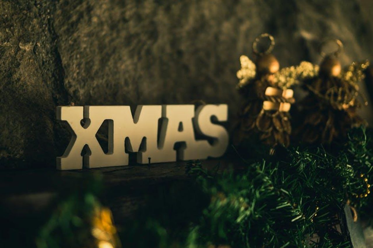 Il_saluto_strano_di_Holly_QzOe2k9YRv - Confidenze24 Source: Francesco Paggiaro - pexels - Close-up of festive Christmas decorations featuring a 'XMAS' sign and gold ornaments.