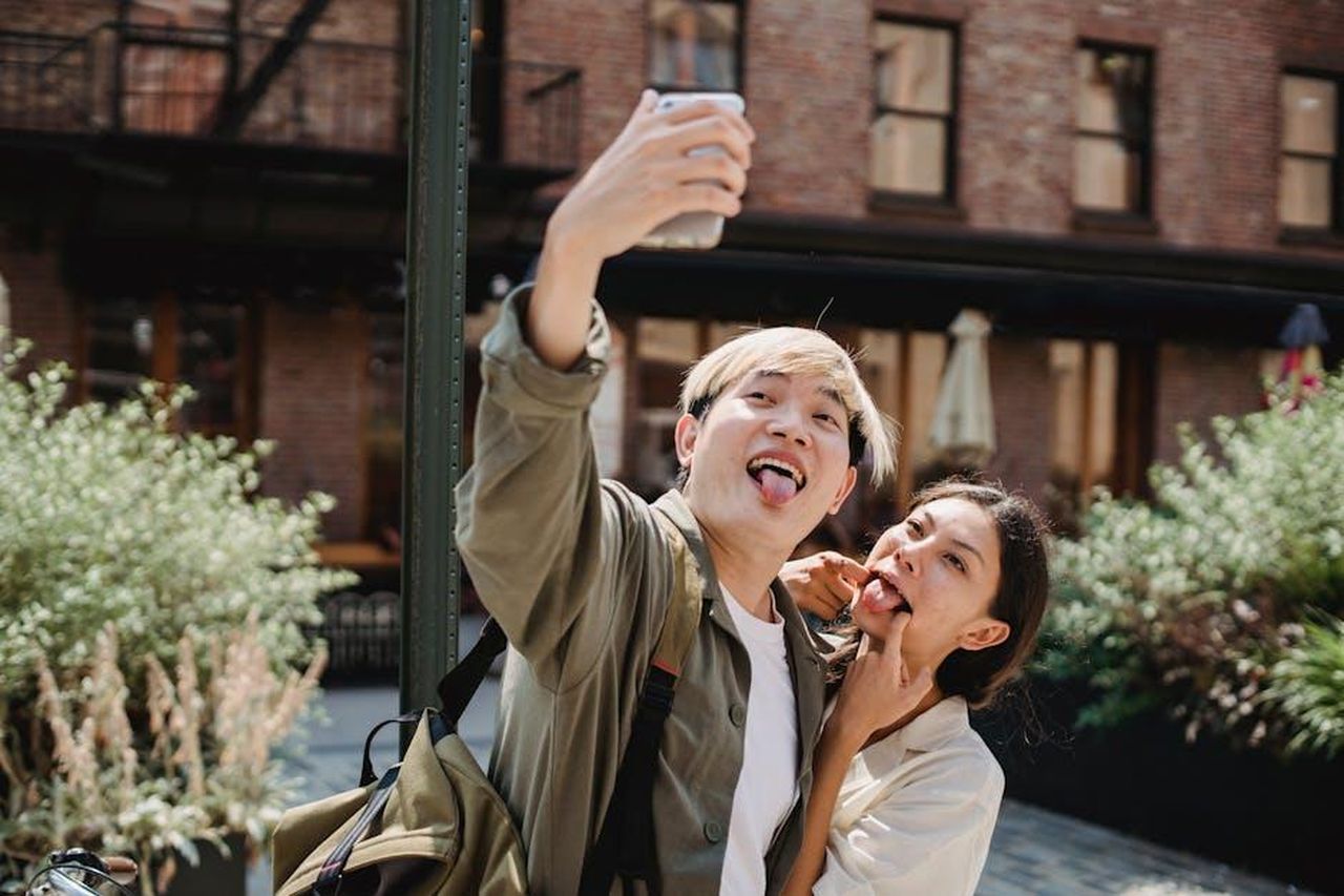 Il_selfie_che_fa_sognare_i_fan_BBZt56nKFr - Confidenze24 Source: Samson Katt - pexels - Playful young couple sticking tongues out while taking an outdoor selfie in a sunny urban setting.