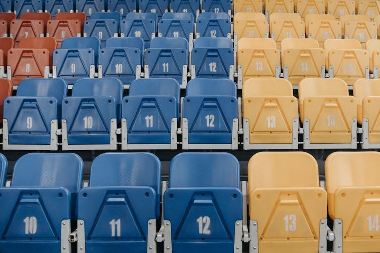 Il_significato_del_numero_12_nel_mondo_di_Taylor_n07oGjiZtK - Confidenze24 Source: Pavel Danilyuk - pexels - Uniform rows of red, blue, and yellow stadium seats with numbers visible.