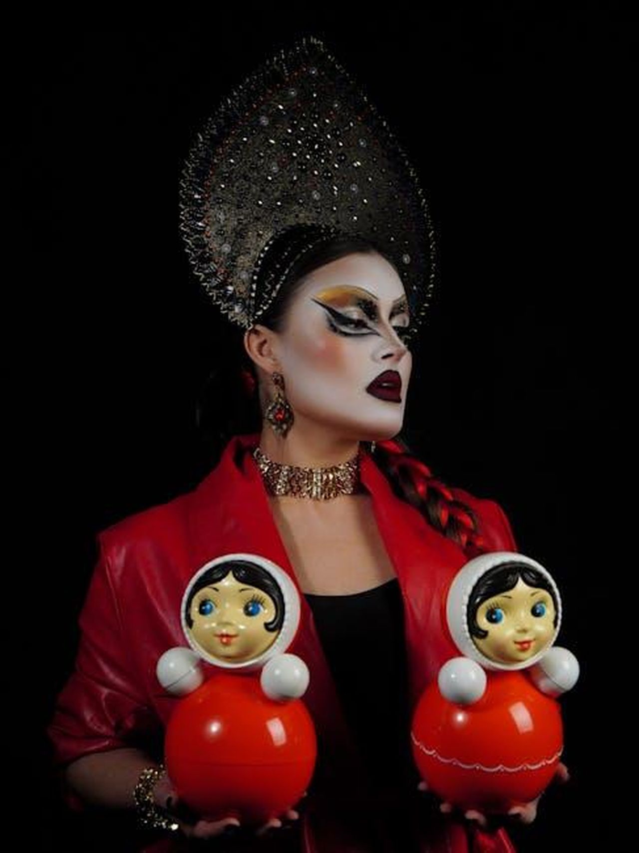 Il_sogno_di_Vivian_di_partecipare_al_mondo_del_drag_4h2As8YOKE - Confidenze24 Source: Nadin Sh - pexels - Drag queen in elaborate costume holding two traditional Russian dolls against a dark backdrop.
