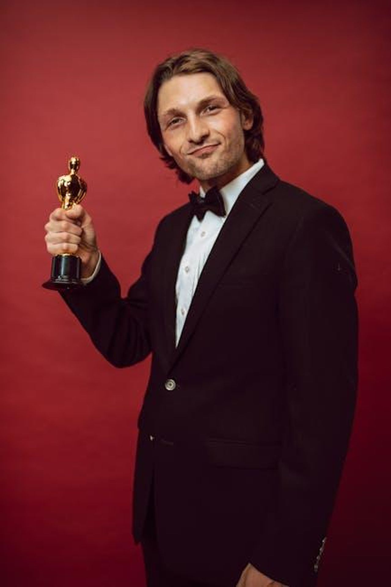 Il_successo_di_Patrick_Schwarzenegger_w4Hrb7HRLT - Confidenze24 Source: RDNE Stock project - pexels - A man in formal attire proudly holds a trophy against a red background, symbolizing success and recognition.