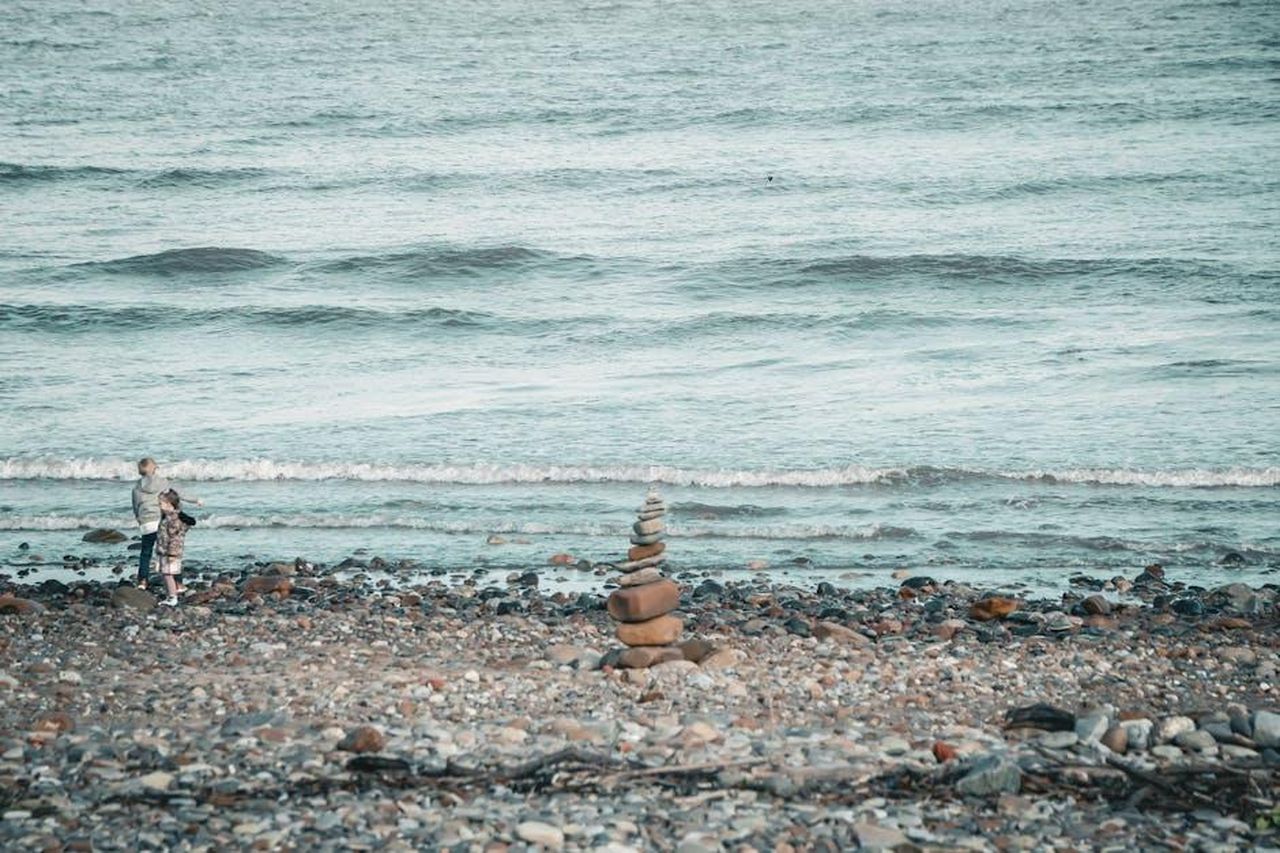 Il_supporto_del_fratello_di_Wendy_3q1mb8tch5 - Confidenze24 Source: Shuo Wang - pexels - Two children playing on a pebble beach with stone cairn stacks in the foreground.