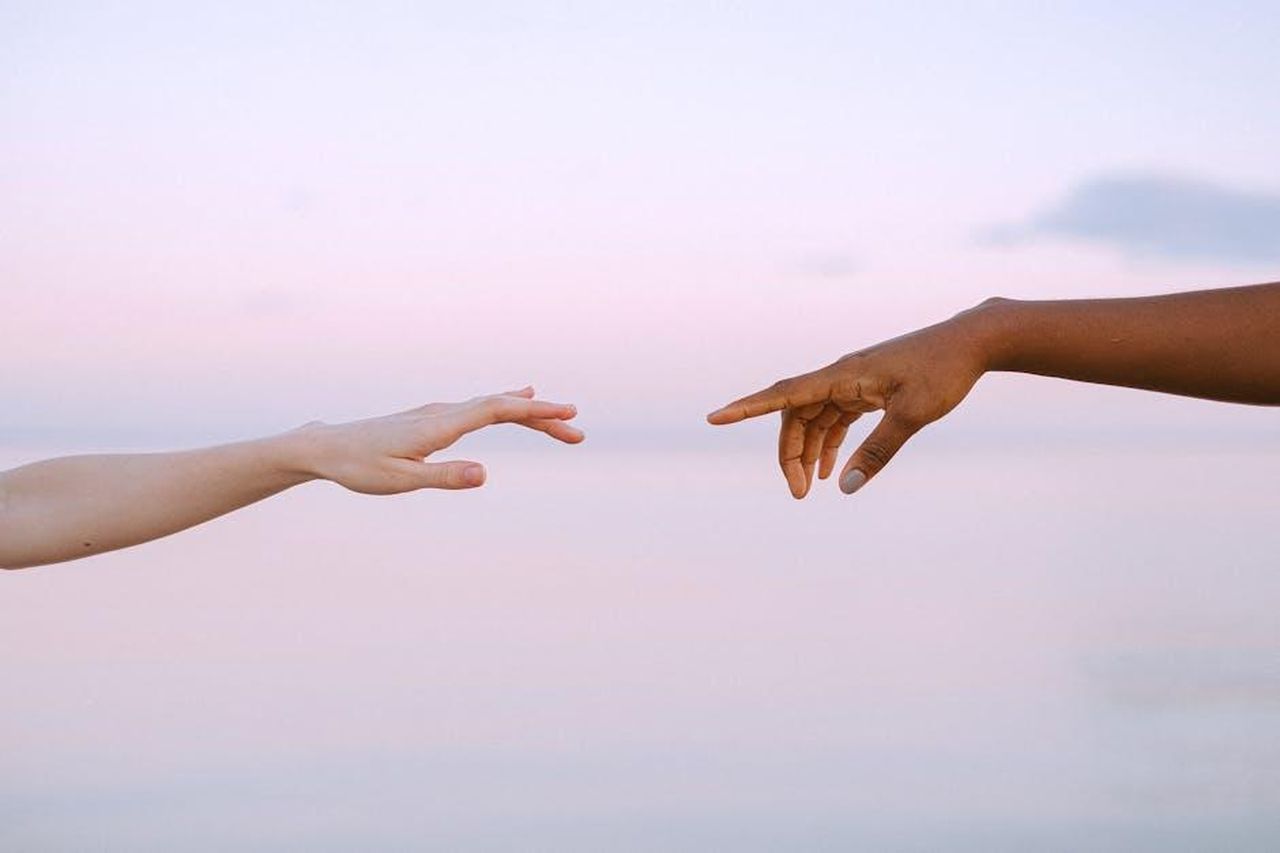 Il_supporto_di_amici_e_colleghi_nel_settore_olIeT8SzHa - Confidenze24 Source: Anna Shvets - pexels - Two diverse hands reaching out across a pastel horizon, symbolizing unity and connection.
