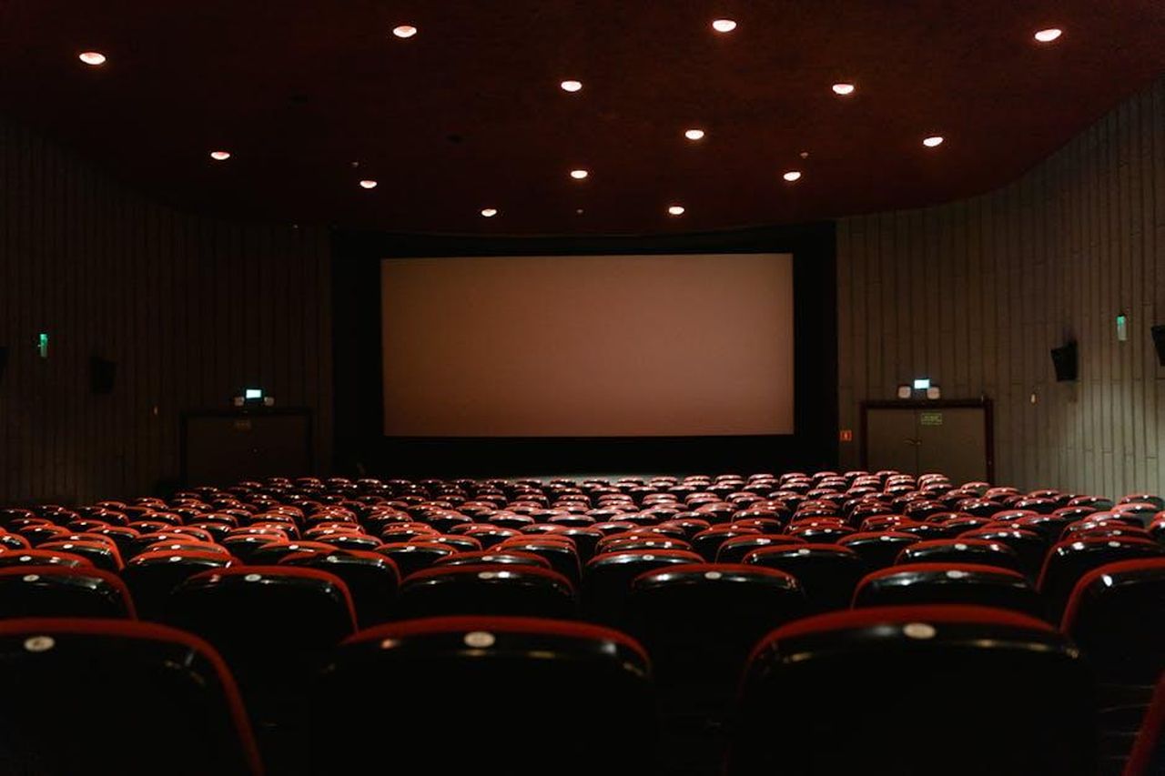 Il_tumulto_di_Blake_Lively_e_Justin_Baldoni_rTBGqxfac3 - Confidenze24 Source: Tima Miroshnichenko - pexels - A dimly lit empty cinema theater with rows of red chairs facing a projector screen.