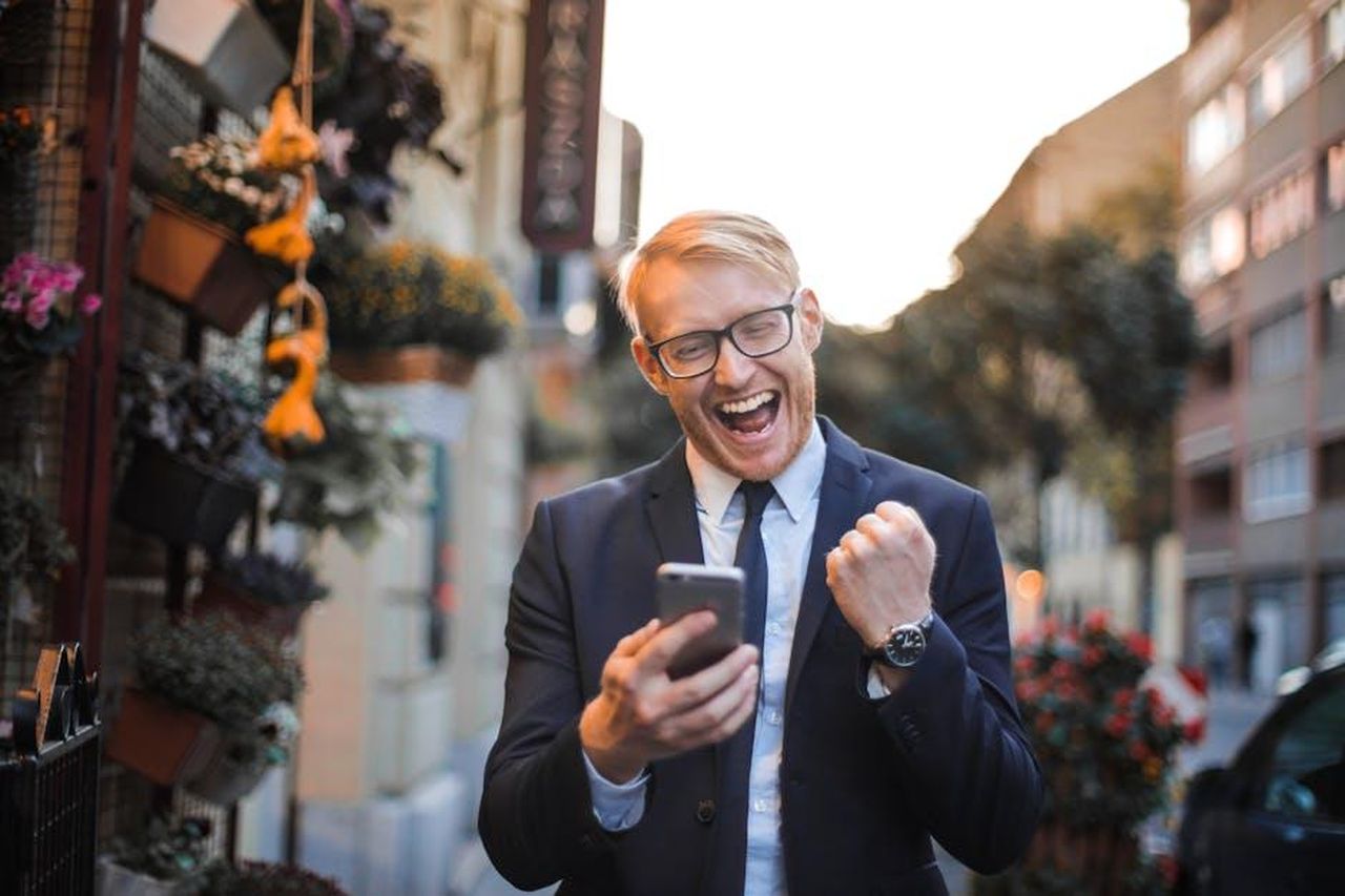 Il_vedovo_di_Paul_rivela_buone_notizie_haVUdbo0gg - Confidenze24 Source: Andrea Piacquadio - pexels - A joyful man in a suit celebrates good news on his smartphone in an urban street setting.