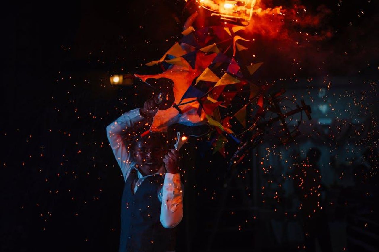 Il_verdetto__arrivato_AZBrHrnNbz - Confidenze24 Source: Fernando Capetillo - pexels - Vibrant fire show at night featuring a performer amidst colorful flags and sparks.