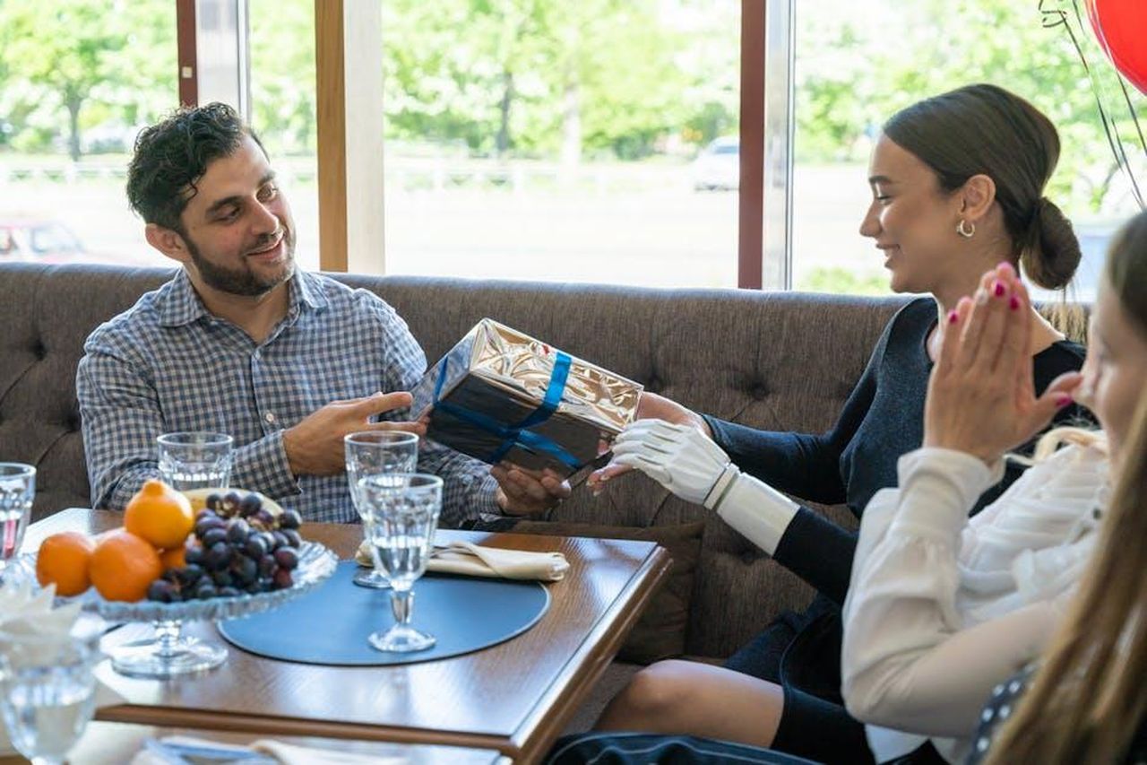 Incontro_con_David_BhmH8Rwpq5 - Confidenze24 Source: Mikhail Nilov - pexels - Smiling friends exchanging a gift in a cozy indoor setting, symbolizing joy and togetherness.
