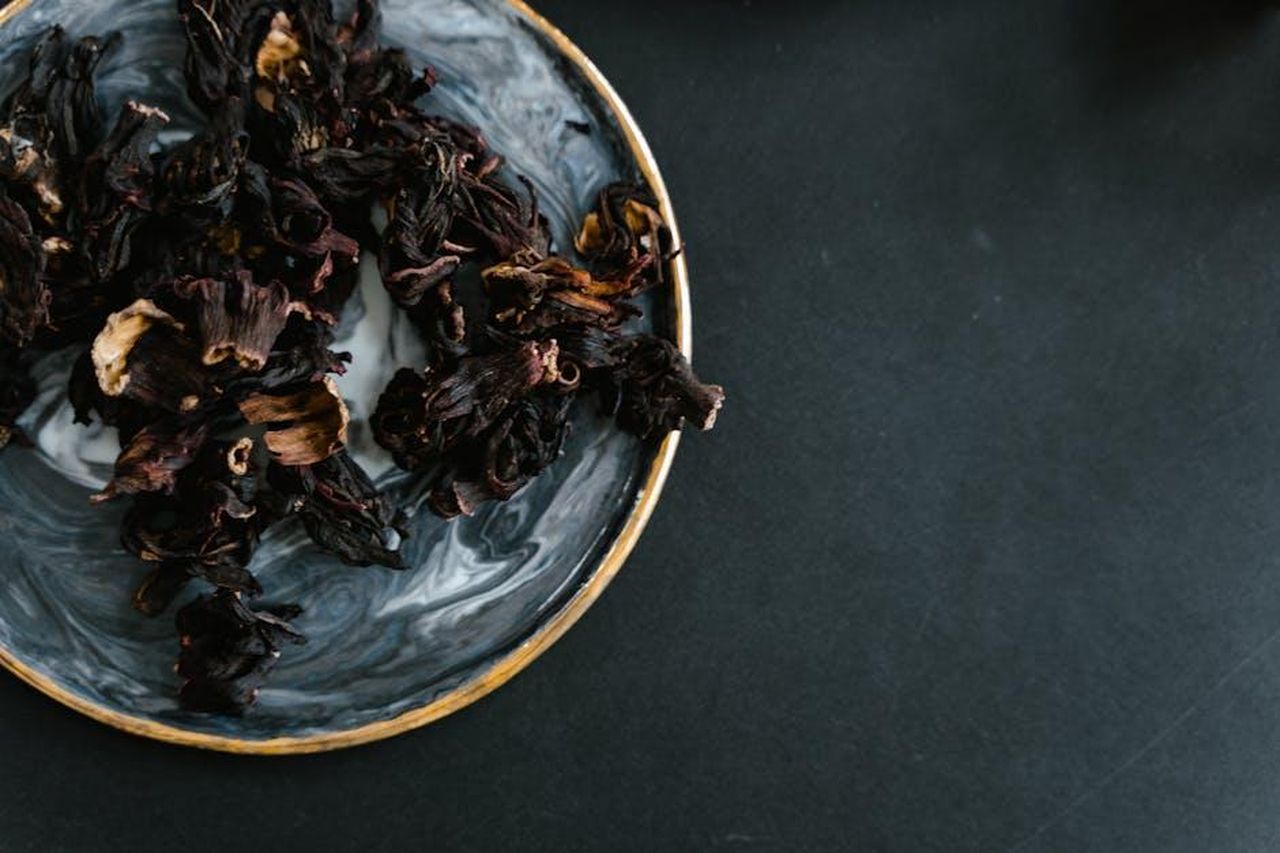 Ingredienti_e_benefici_del_prodotto_31ojXk3ycf - Confidenze24 Source: MART PRODUCTION - pexels - Still life of dry hibiscus flowers in a marble bowl on a dark background.