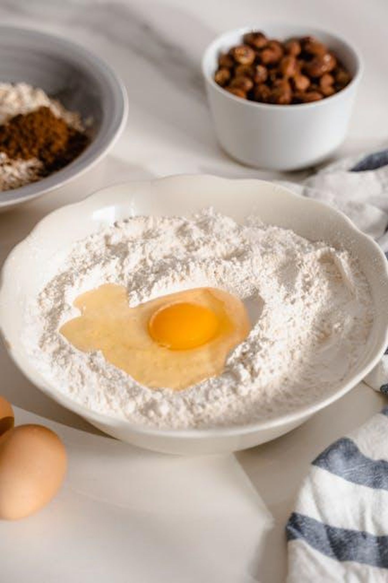 Ingredienti_e_preparazione_della_Torta_di_Carote_QRLpKl3XfB - Confidenze24 Source: MART PRODUCTION - pexels - A fresh egg nestled in flour amidst baking ingredients.