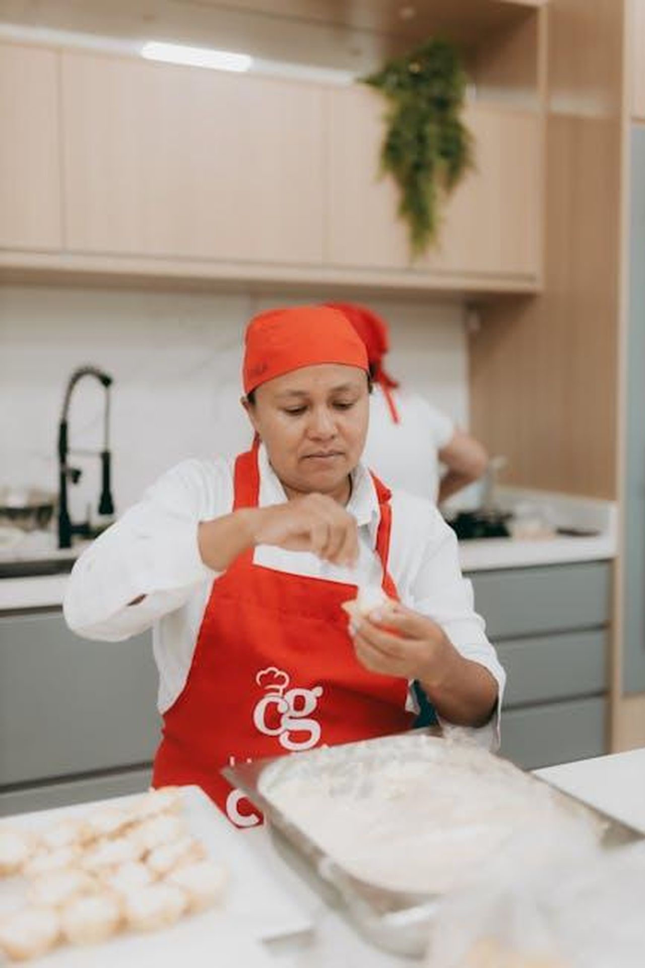 Ingredienti_e_preparazione_della_torta_al_cioccolato_MYn08Fu8Jm - Confidenze24 Source: Alexander Mass - pexels - Chef expertly handling dough in a modern kitchen setting, wearing a red apron and headscarf.