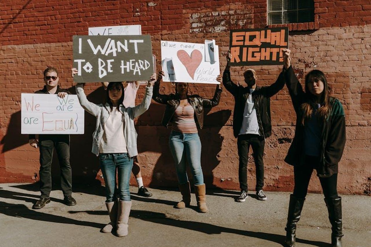 Interviste_e_storie_di_vita_cambiate_O3KR15TCB7 - Confidenze24 Source: RDNE Stock project - pexels - Diverse group holding protest signs for equality and peace near a brick wall.