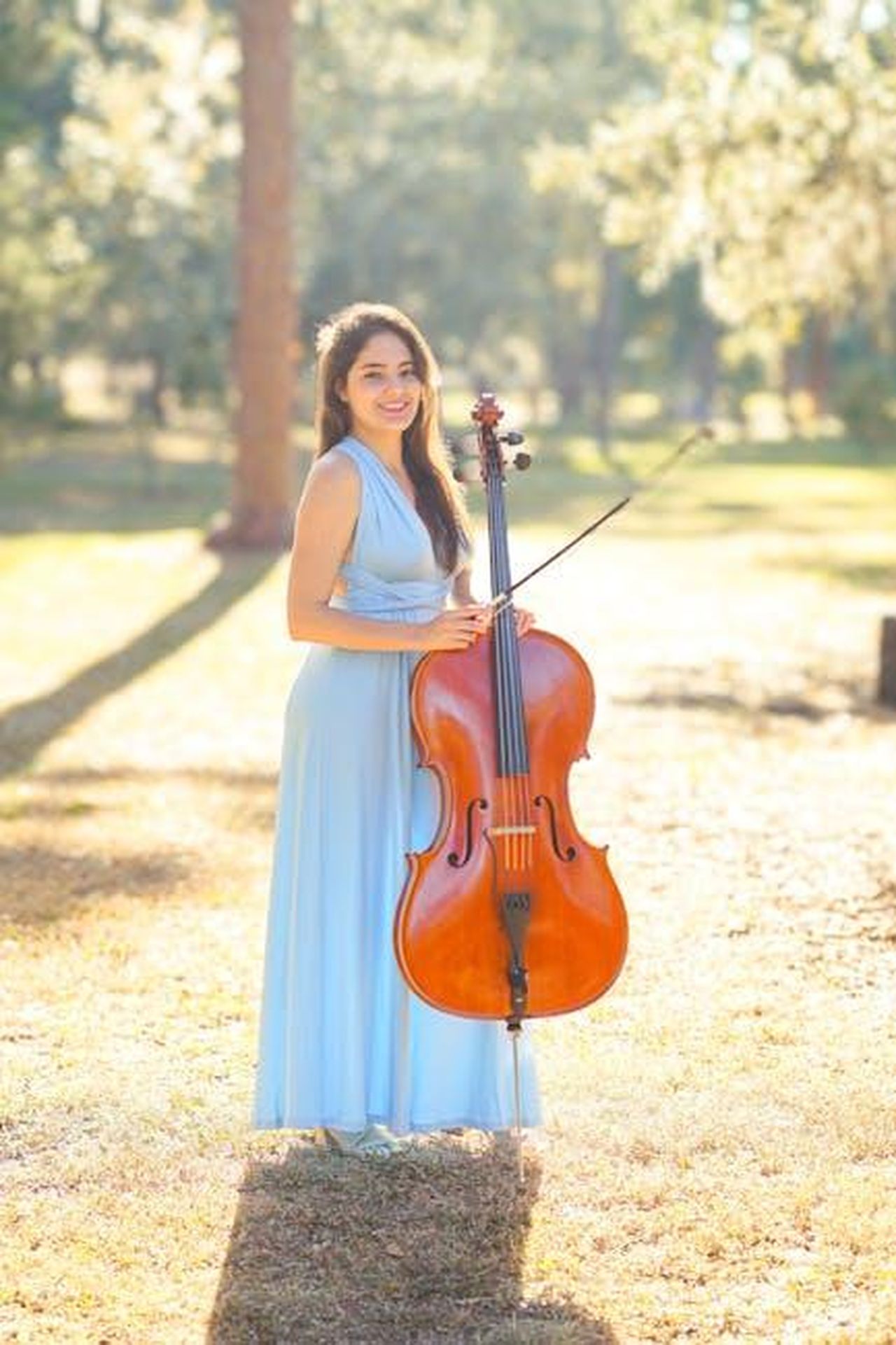 Jagger_e_la_sua_passione_per_la_musica_YeCiyw4SCI - Confidenze24 Source: Anthony Simmons - pexels - Elegant woman in blue gown playing cello outdoors under sunlit trees, embracing music and nature.