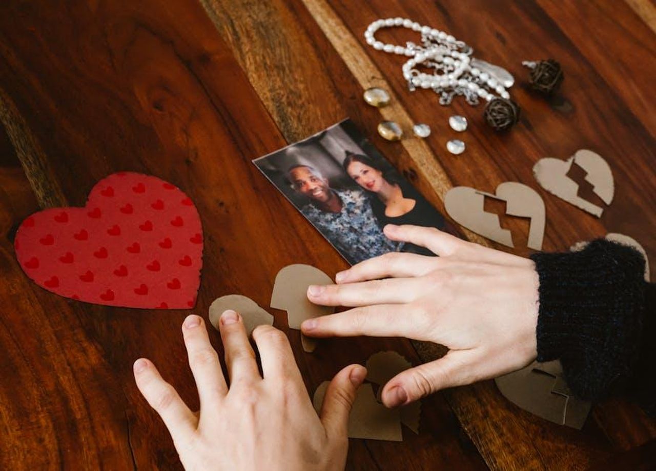 Jamie_e_Louise_vanno_avanti_mkqUN9o3va - Confidenze24 Source: RDNE Stock project - pexels - Close-up of hands arranging broken hearts near a couple's photo on a wooden table.