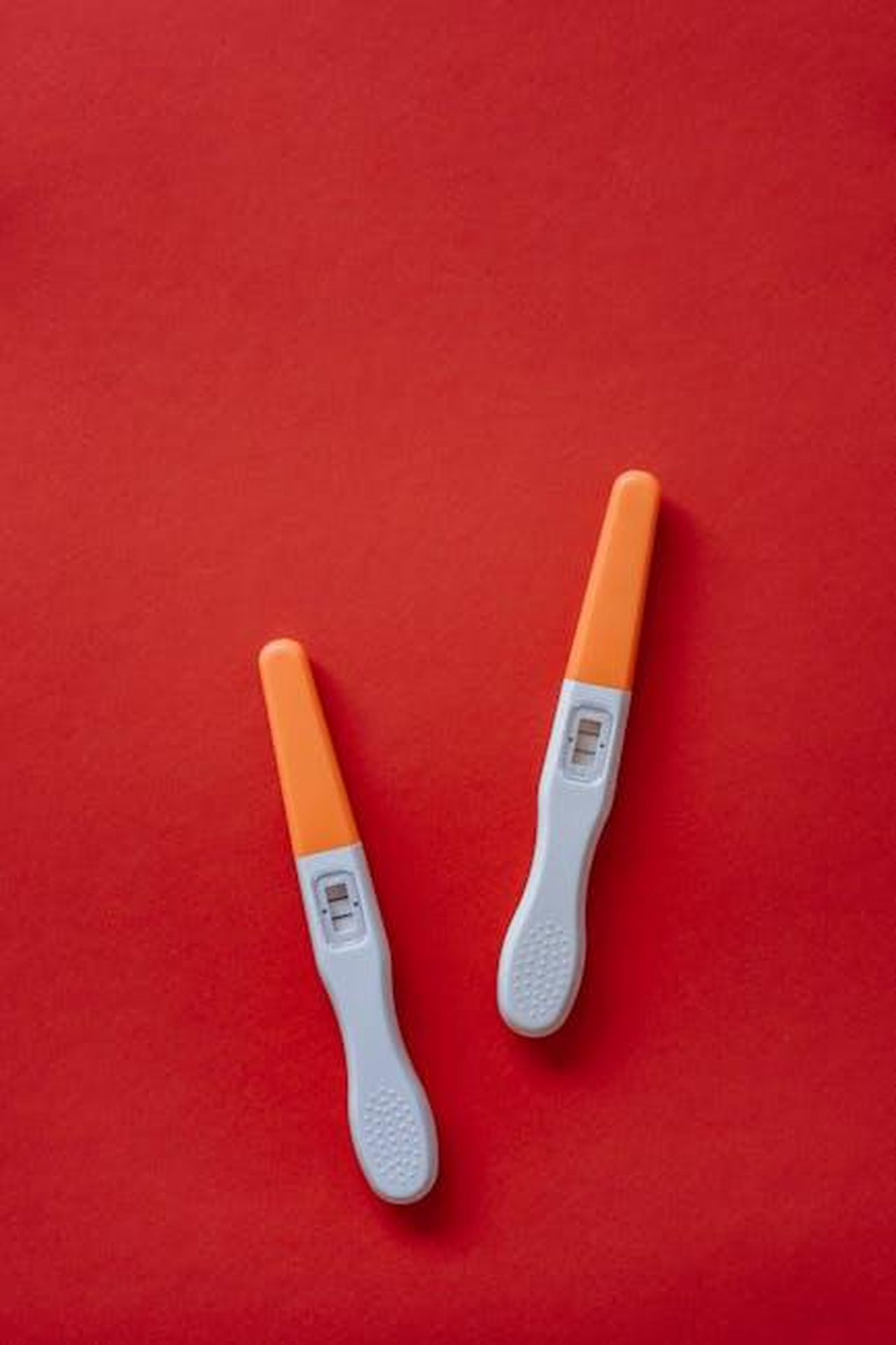 Jesy_e_Zion_aspettano_gemelli_GpJwWWd7lc - Confidenze24 Source: olia danilevich - pexels - Two pregnancy tests displayed on a bold red surface, photographed as a flat lay.