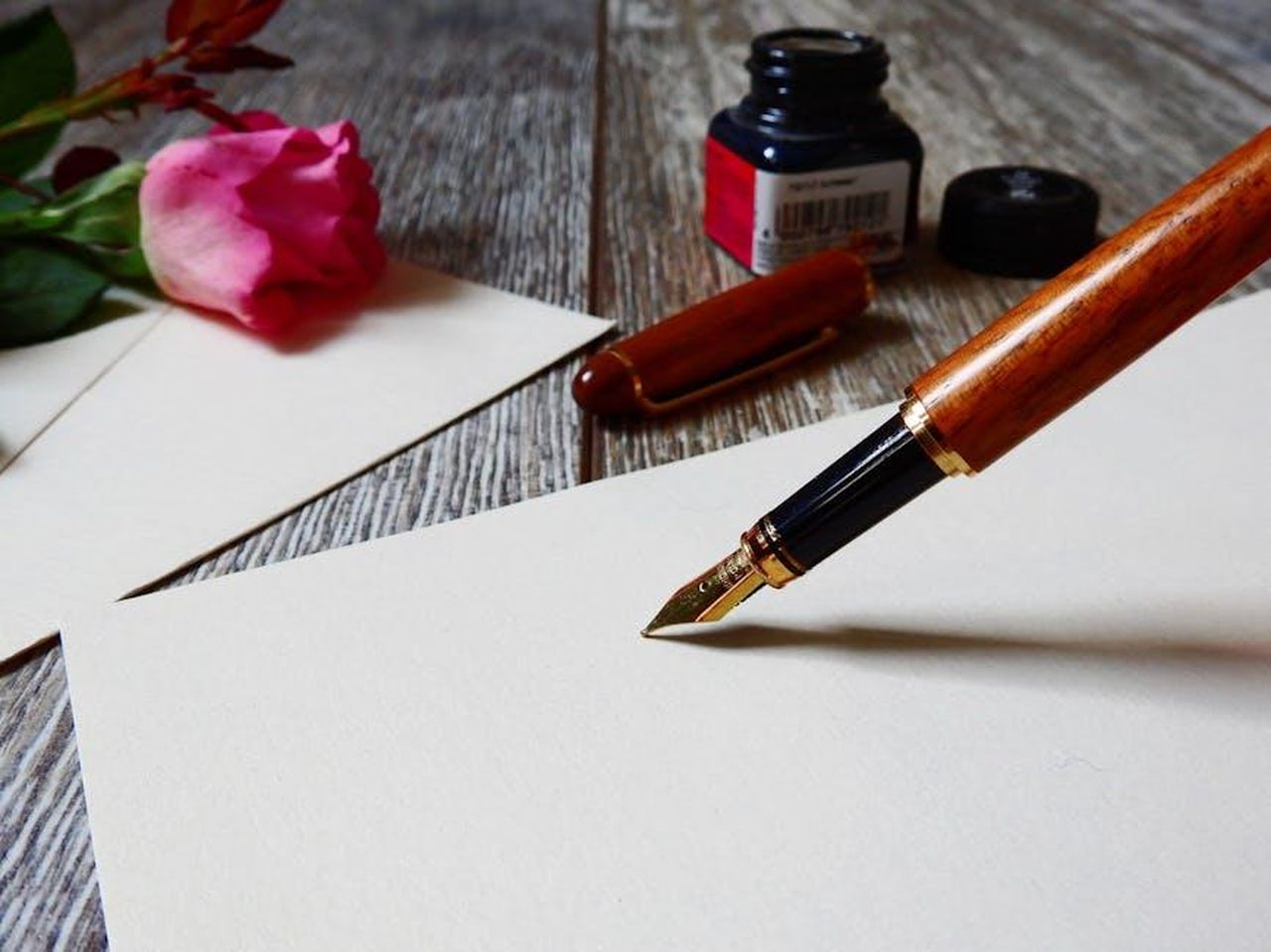 Katharine_Hepburn_e_il_suo_amore_per_Spencer_dwJF173t3b - Confidenze24 Source: Pixabay - pexels - A romantic setup with a rose, fountain pen, and paper, perfect for heartfelt writing.