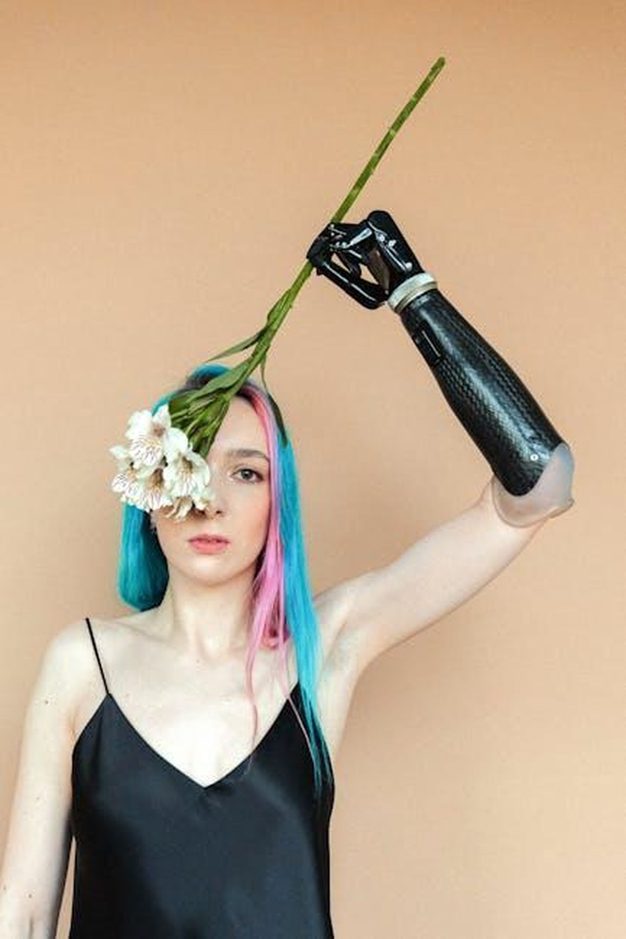 Katie_ottiene_un_occhio_artificiale_hj9Ak8uddr - Confidenze24 Source: Anna Shvets - pexels - Woman with colored hair and prosthetic arm holding flowers, embracing diversity.