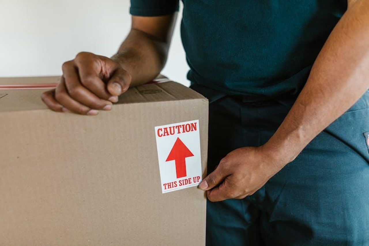Kelsey_Parker_risponde_ai_troll_wIV5mYRvGu - Confidenze24 Source: RDNE Stock project - pexels - A person handling a moving box with a 'caution this side up' label indoors.
