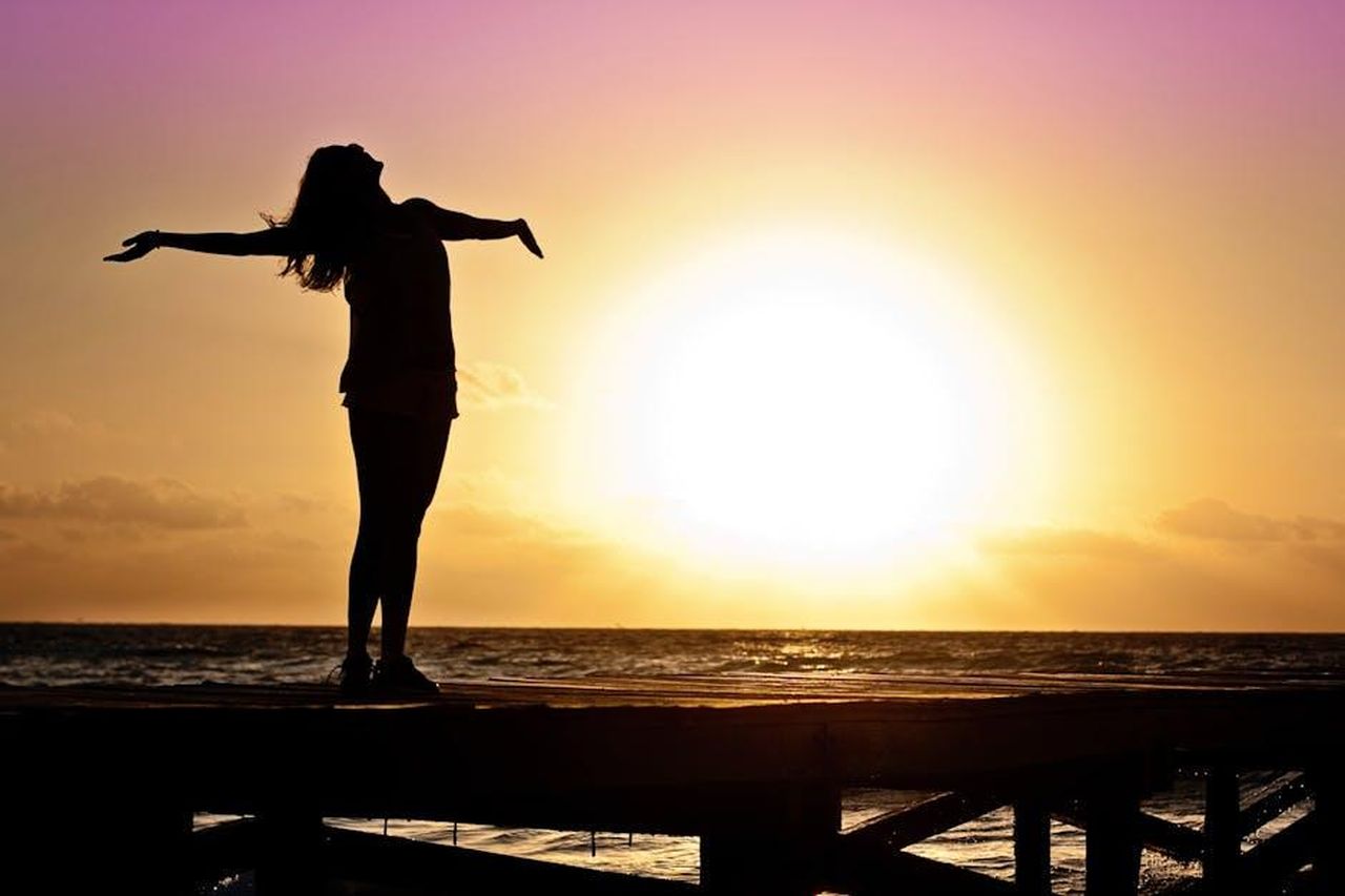 Kym_sta_godendo_la_sua_libert_pQdga8KOIf - Confidenze24 Source: Jill Wellington - pexels - A joyful silhouette of a woman standing on a dock at sunset, embracing the freedom of nature.