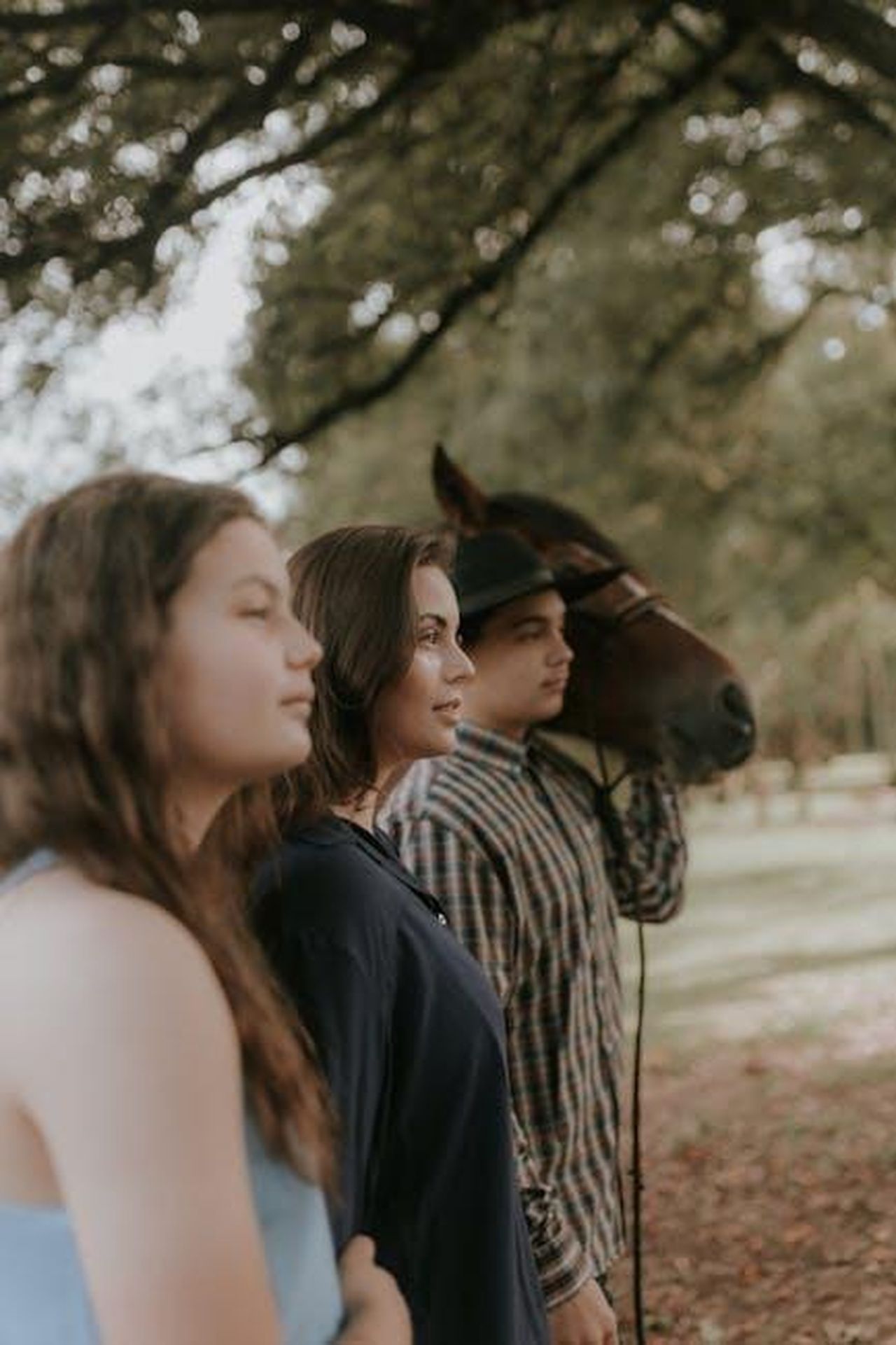 La_Dinamica_Familiare_j5JJhGdVbP - Confidenze24 Source: Alexander Mass - pexels - A serene family portrait featuring two women and a man with a horse under lush trees.
