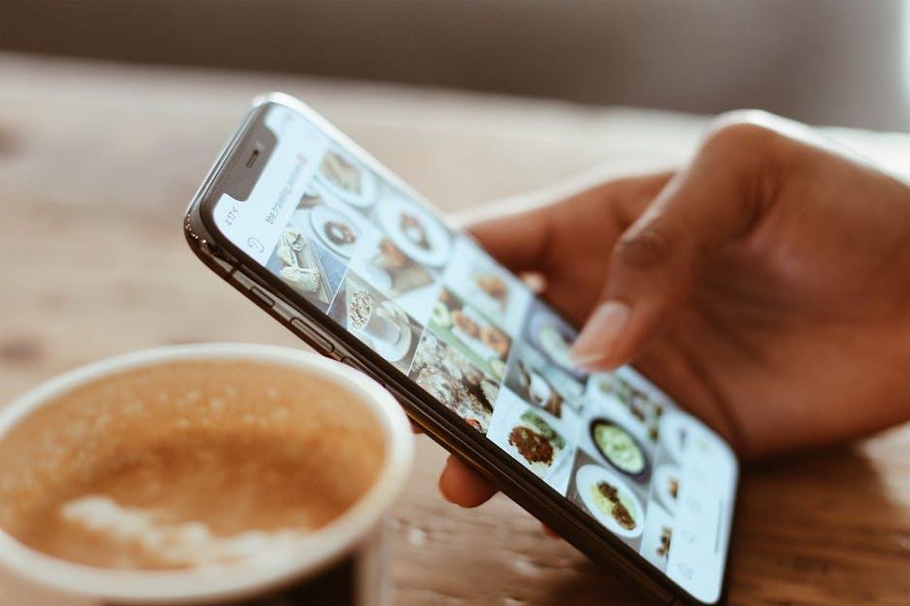 La_Reazione_di_Nikki_sui_Social_Media_ajZPS2spVT - Confidenze24 Source: Kerde Severin - pexels - Hand browsing social media photos on a smartphone next to a cup of coffee indoors.
