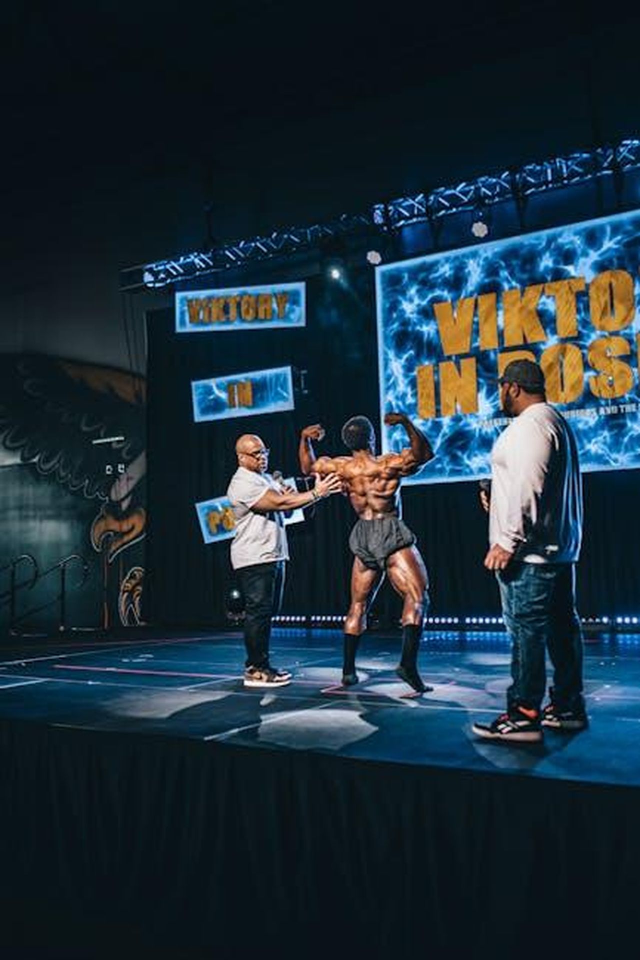 La_Reazione_di_Stephen_A_Smith_NvDvTMOogz - Confidenze24 Source: Ushindi Namegabe - pexels - Muscular bodybuilder posing shirtless on stage during a competition with hosts present.